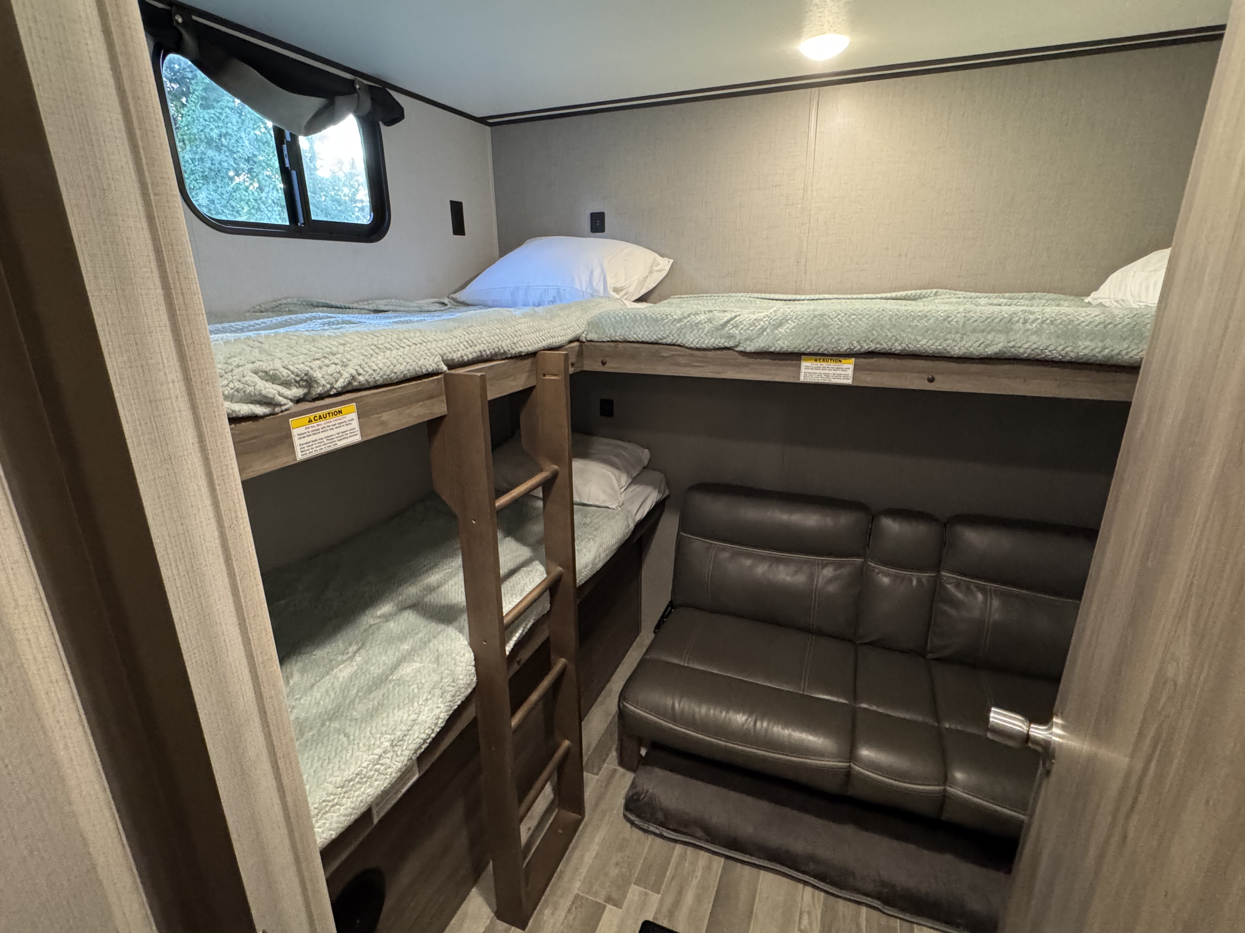 RV rental bunk room: three single bunk beds with soft green blankets, a ladder, and a leather-look gray sofa.. Crossroads RV Zinger 2020