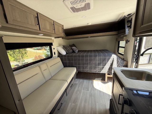Modern RV rental interior with a cozy bed, sofa, kitchenette, and overhead cabinets. Ideal for road trips.. Grand Design Transcend One 2025
