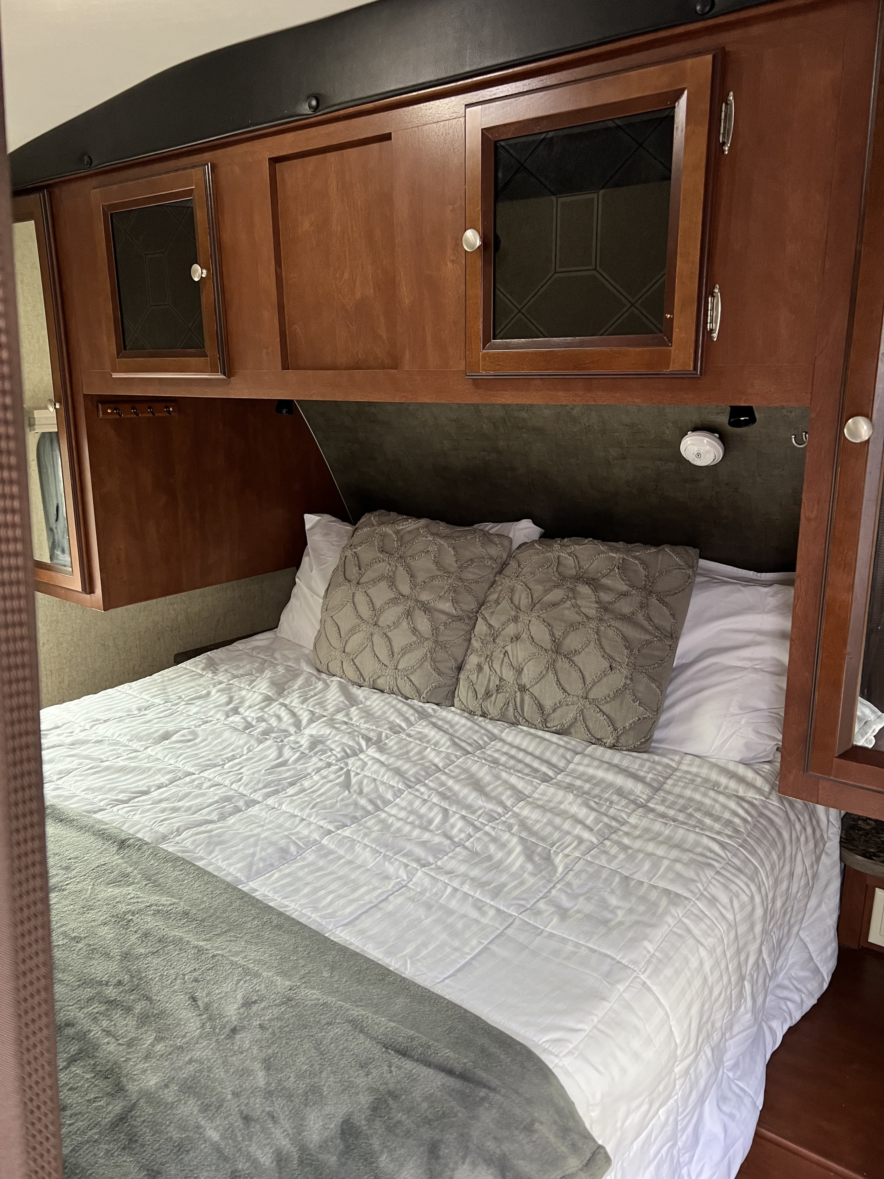 Cozy rv rental bedroom showing a bed with white bedding, grey pillows, and wooden overhead cabinets for storage.. Heartland RVs Mallard 2014