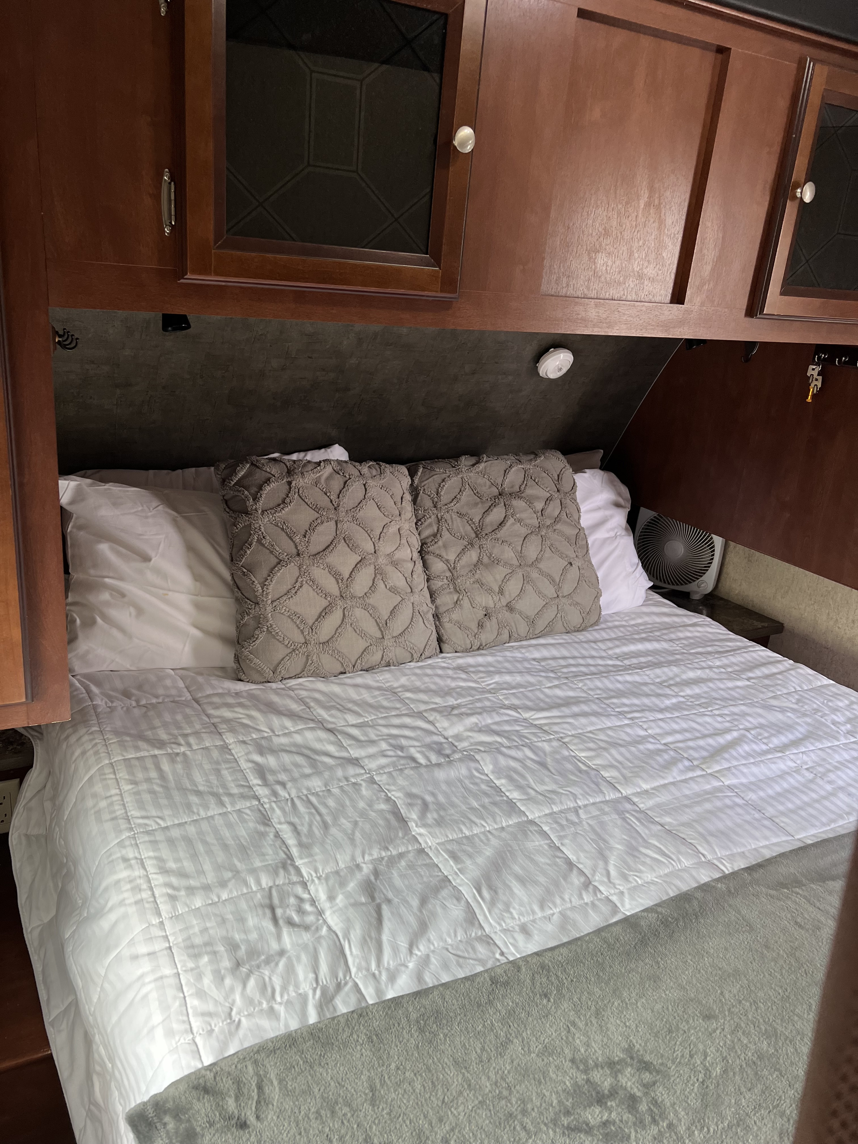 Cozy RV rental bedroom with a white bed, two textured gray pillows, and dark wood overhead cabinets, designed for compact living.. Heartland RVs Mallard 2014