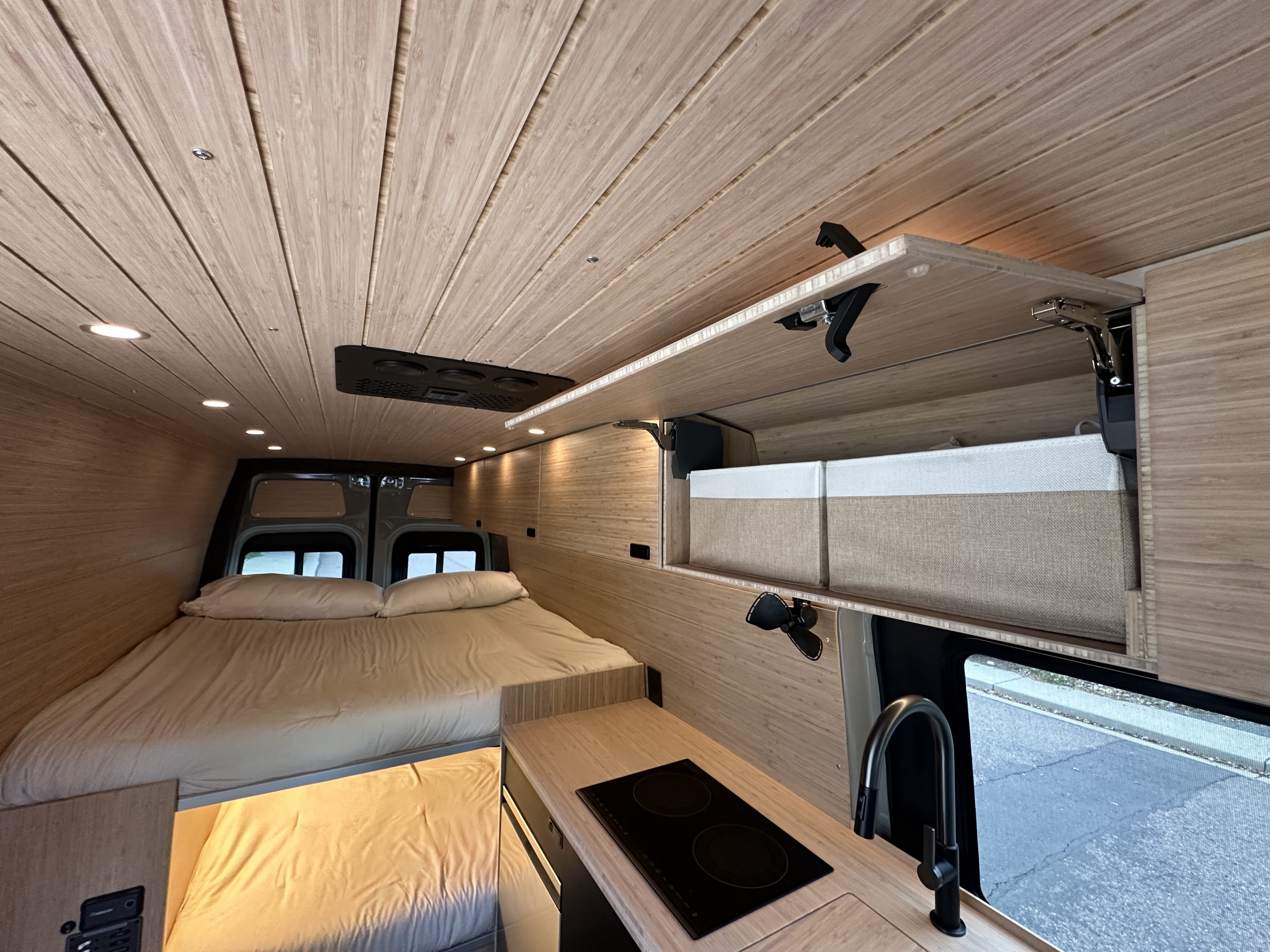 RV rental van interior featuring a cozy bed, compact kitchen, and overhead storage, designed for comfortable travel.. Mercedes-Benz Sprinter 2025