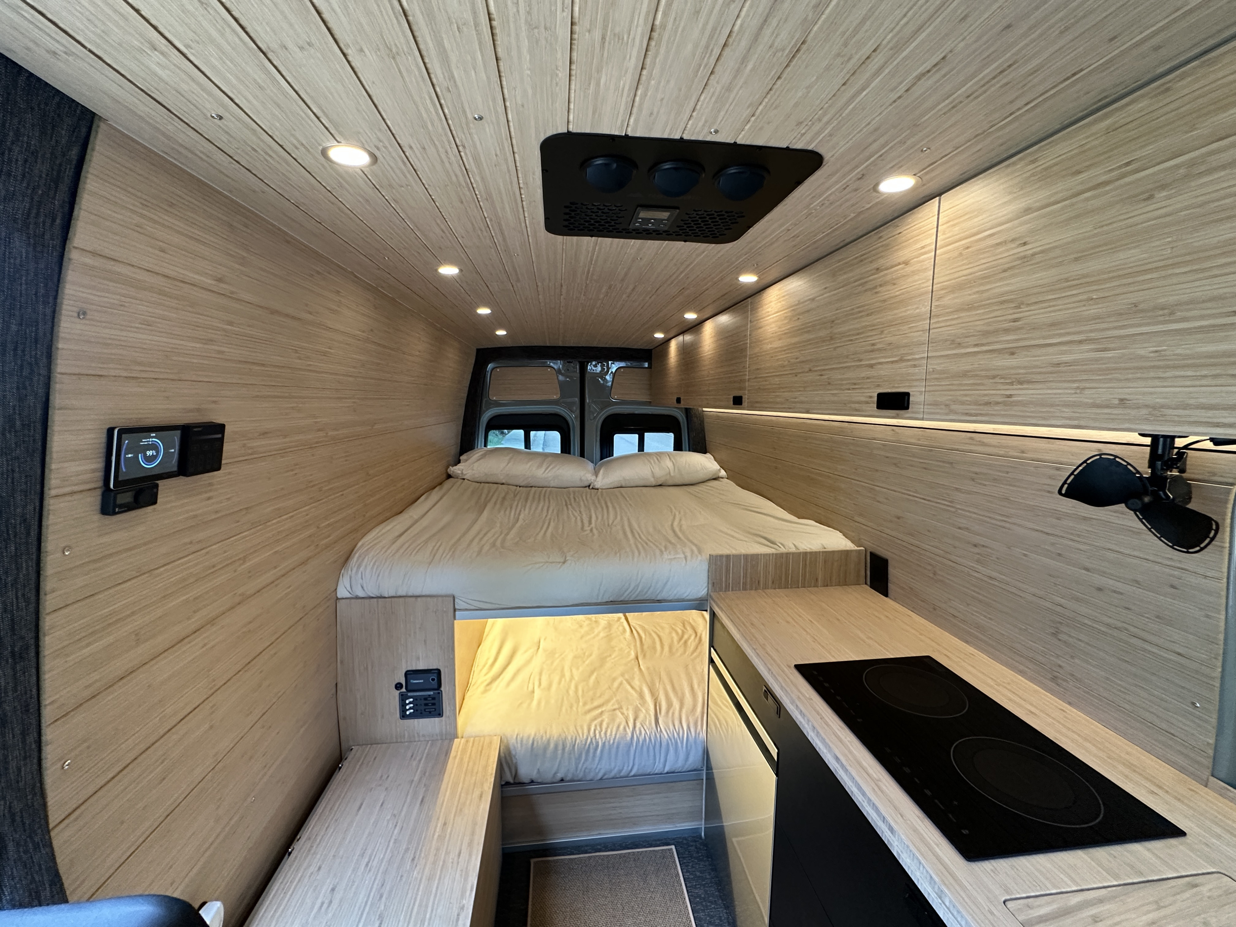 Modern RV rental interior with a cozy bed, sleek kitchen, and light wood paneling, perfect for adventure.. Mercedes-Benz Sprinter 2025