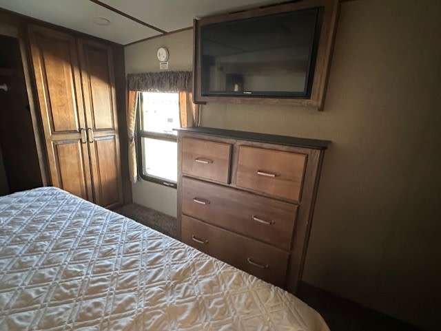 Cozy RV rental bedroom featuring a bed, wooden dresser, mounted TV, and built-in wardrobe for comfort and storage.. Keystone RV Laredo 2018