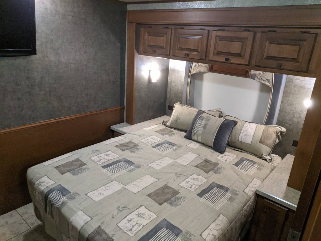 Cozy RV rental bedroom featuring a comfortable bed with patterned bedding, overhead storage, side tables, and a wall-mounted TV.. Allegro Allegro Motorhome 2011