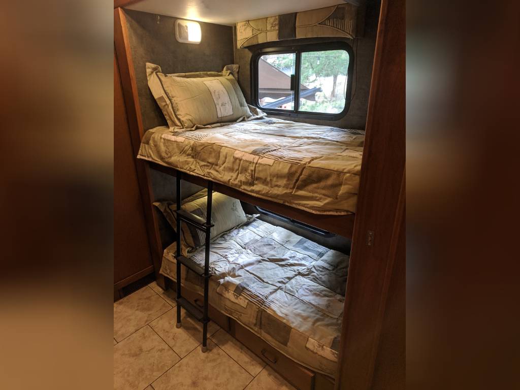 Interior of an RV rental: two bunk beds with quilted bedding, a window above the top bunk, and a ladder.. Allegro Allegro Motorhome 2011