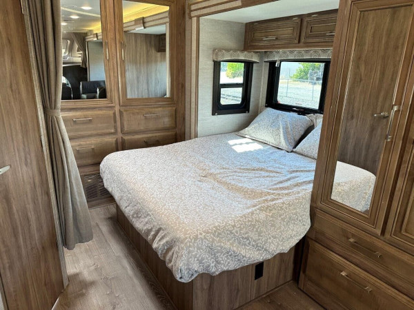 Cozy RV rental bedroom with a comfy bed, windows, and built-in wood cabinets and mirrors. Ideal for travel adventures.. Entegra Coach Odyssey 2021