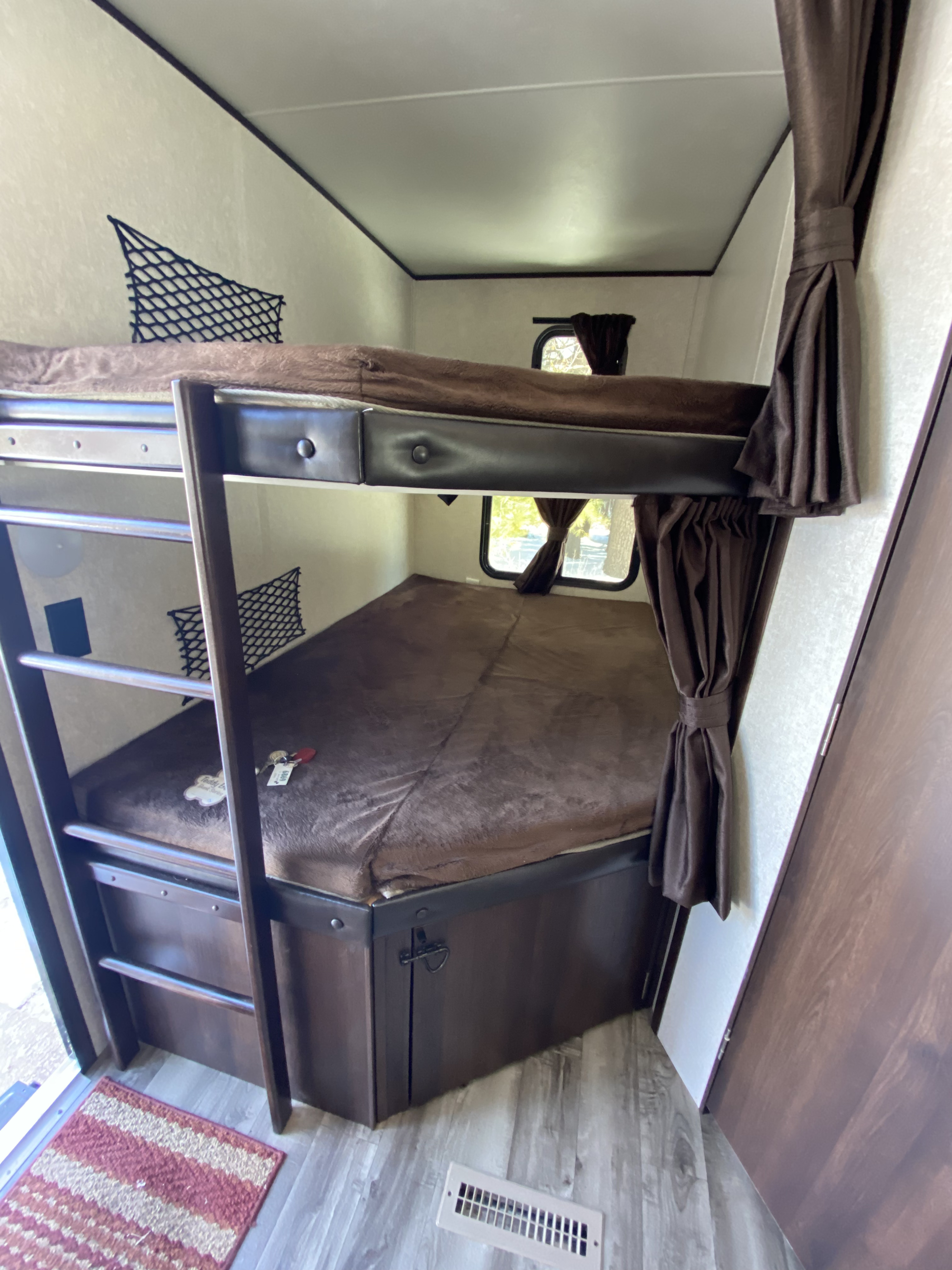 Cozy RV rental interior featuring stacked bunk beds with brown bedding, a ladder, and small windows with curtains.. Jayco Jay Flight 2019