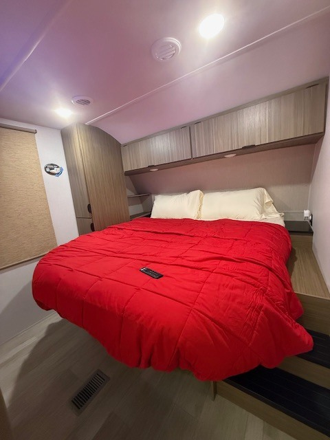 Bright RV rental bedroom features a comfy red bed, overhead storage, and convenient steps. Perfect for travel.. 4X4TWDG2XS8812270 Forest River Wildwood 2025