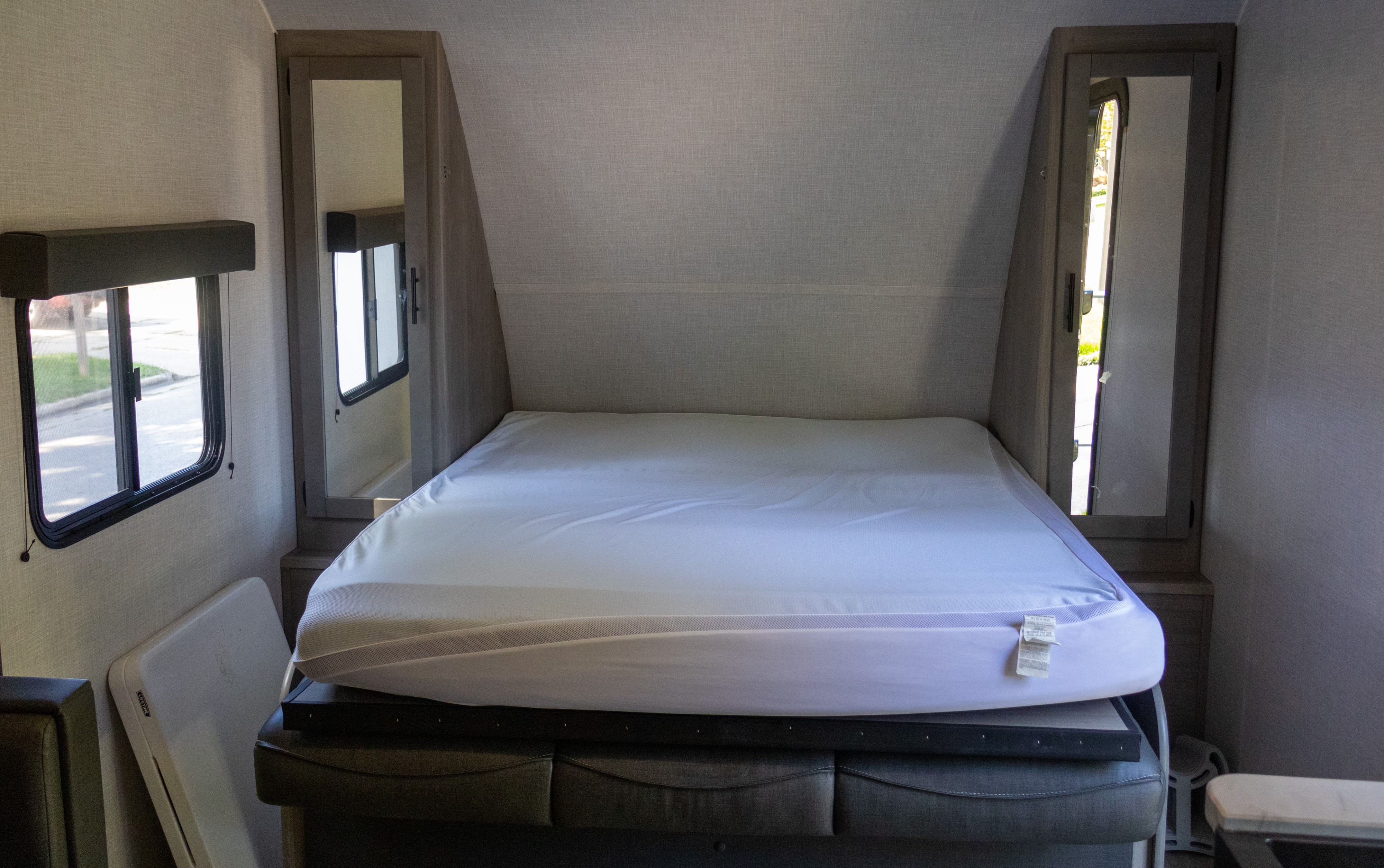RV rental sleeping area with a neatly made bed, side windows, and mirrored wall cabinets for practical storage.. Dutchmen Coleman Light 2023