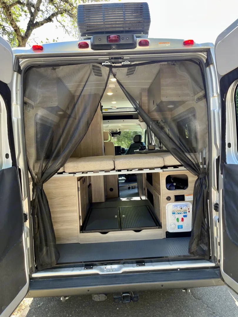 RV rental camper van interior from the rear. Features bug screen, comfortable bed, under-bed storage, and utility panel.. Winnebago Solis 2023