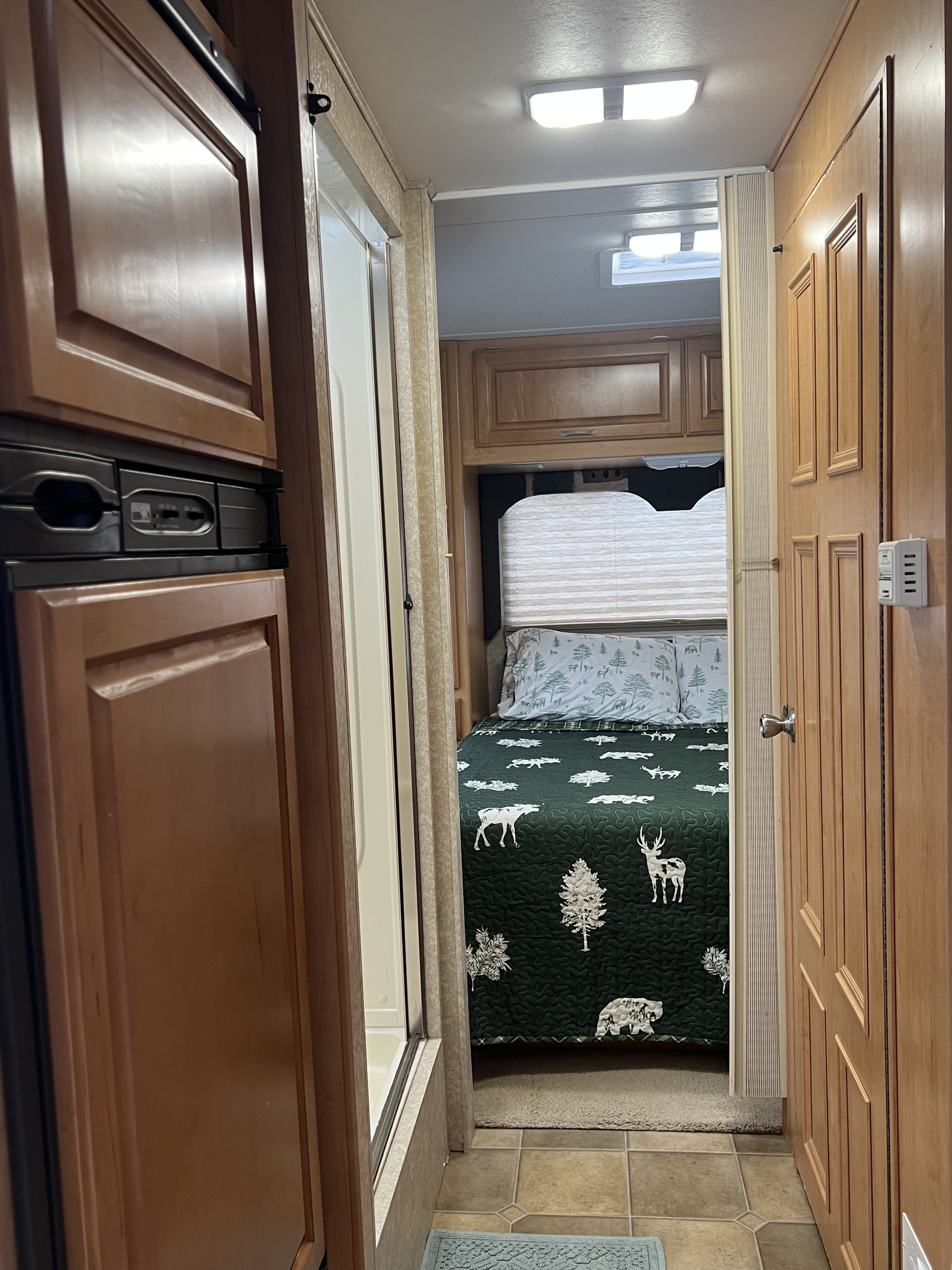 Cozy RV rental interior, showing a bedroom with a nature-themed quilt, cabinetry, refrigerator, and a shower stall in a narrow hallway.. Four Winds 5000 2006