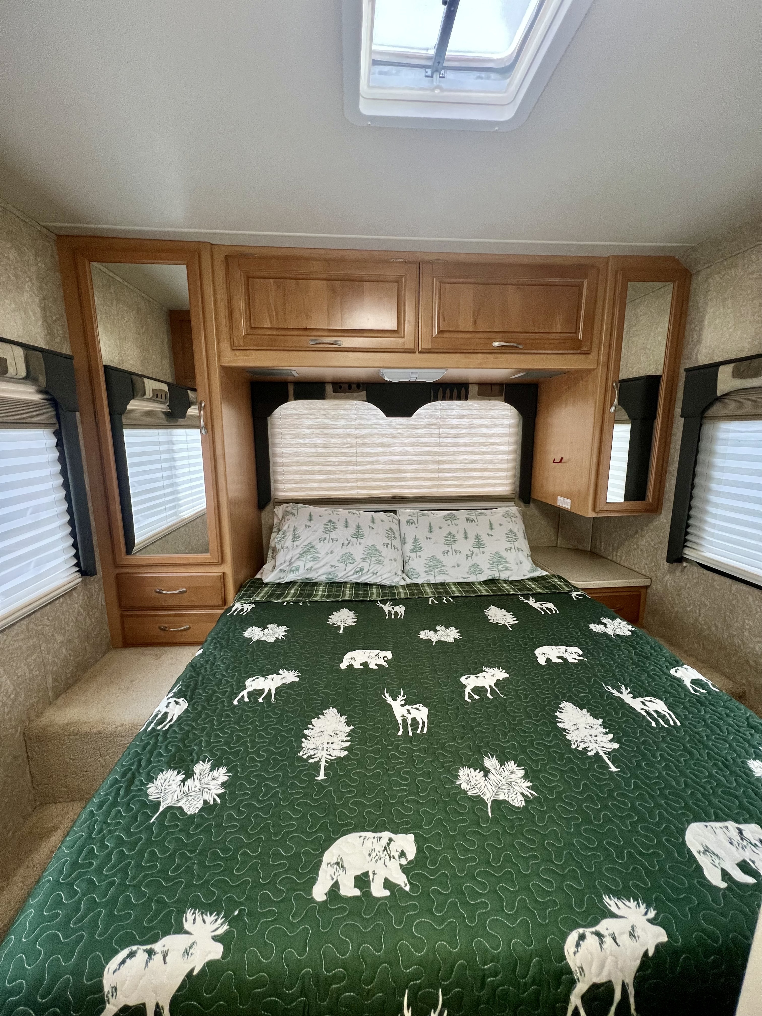 An RV rental bedroom features a green quilt with forest animals & trees, flanked by wood cabinets & mirrors.. Four Winds 5000 2006