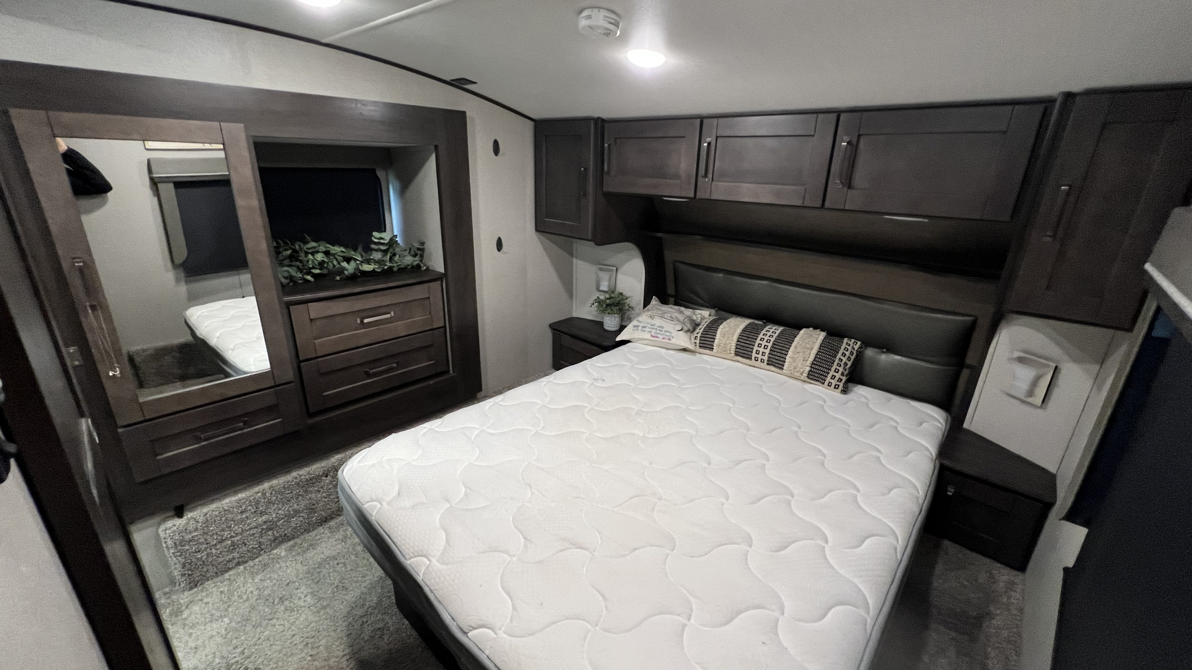 This RV rental features a comfortable bedroom with a queen bed, dark wood cabinetry, and ample storage, perfect for travel.. Grand Design Reflection 2020