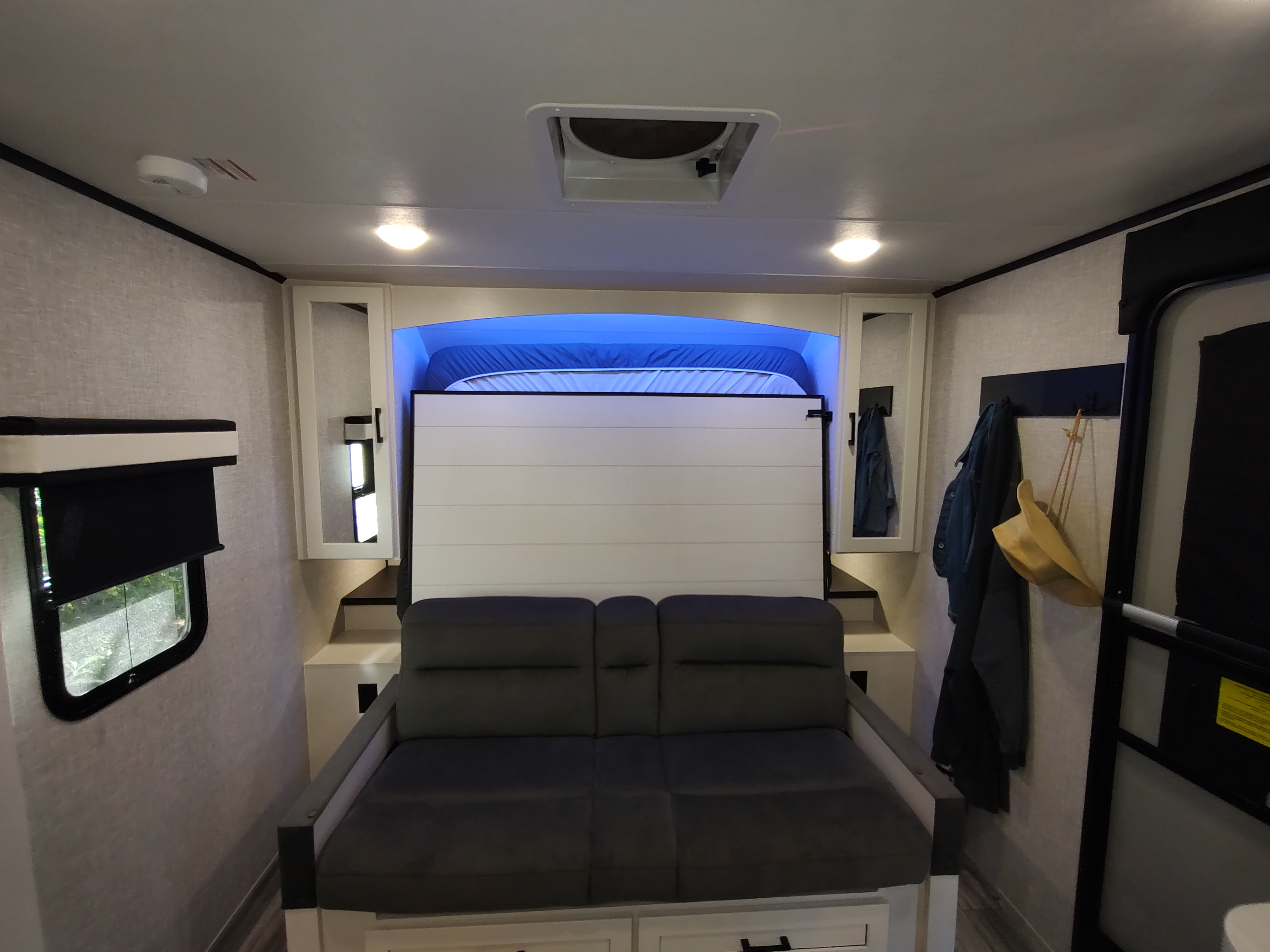 Modern RV rental interior showcasing a convertible sofa and murphy bed with blue lighting, a window, and storage.. Jayco Jay Feather Air 18mbh 2024