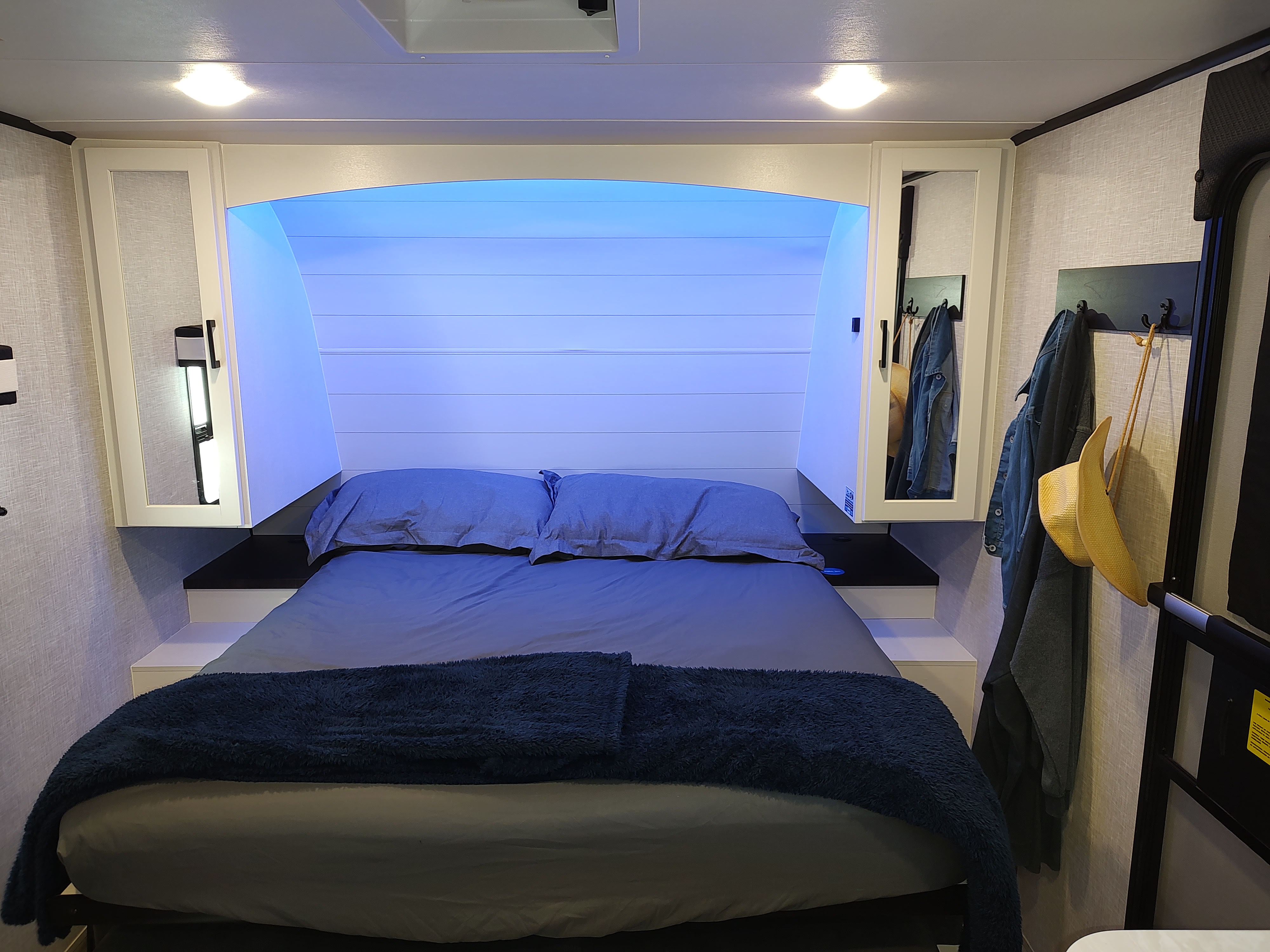 Cozy RV rental bedroom featuring a bed with blue ambient lighting and integrated storage on either side.. Jayco Jay Feather Air 18mbh 2024