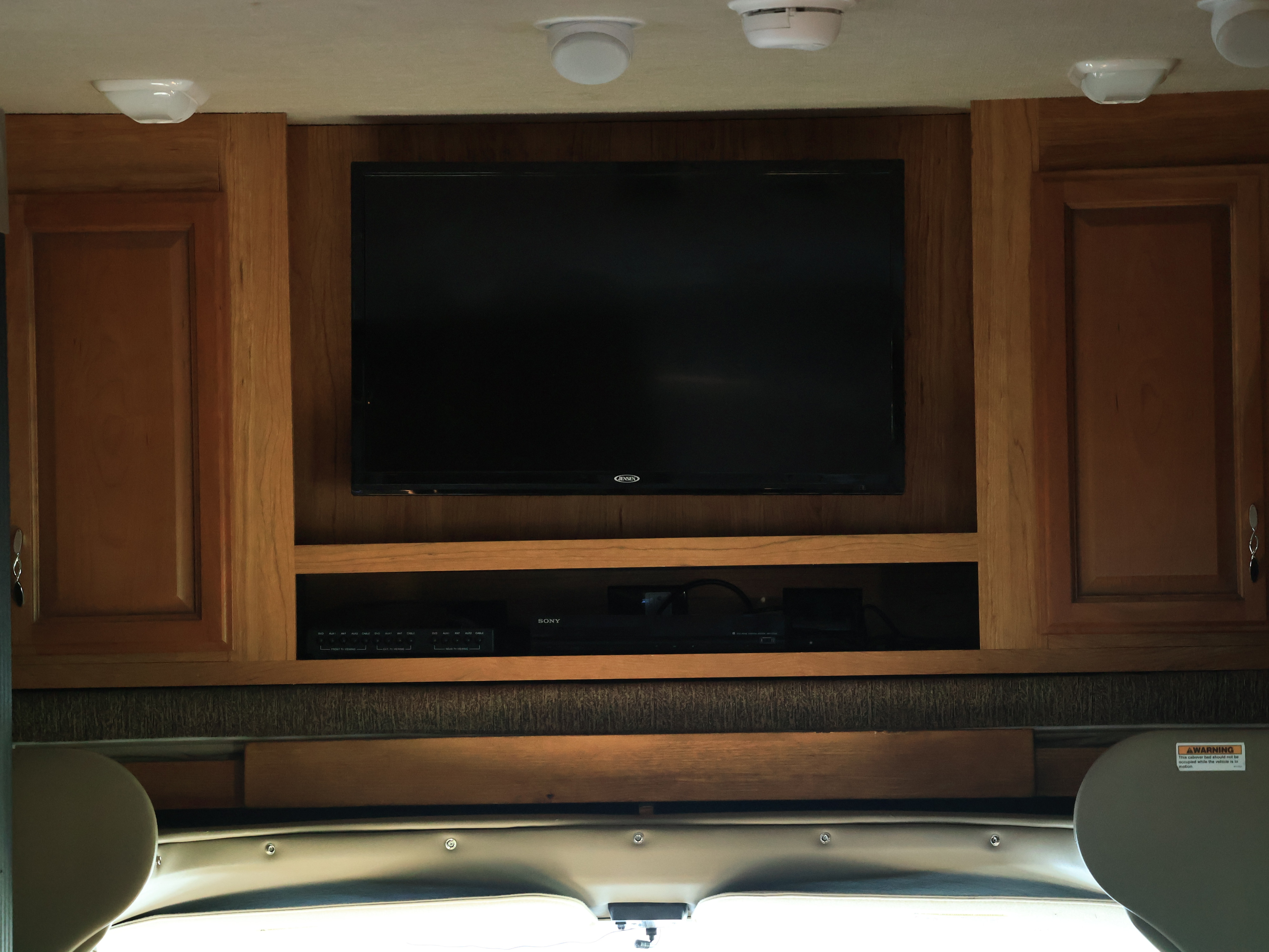 RV rental interior with a wooden entertainment center: TV, Sony player, overhead lights, and a smoke detector on the ceiling.. Jamboree Sport 2015