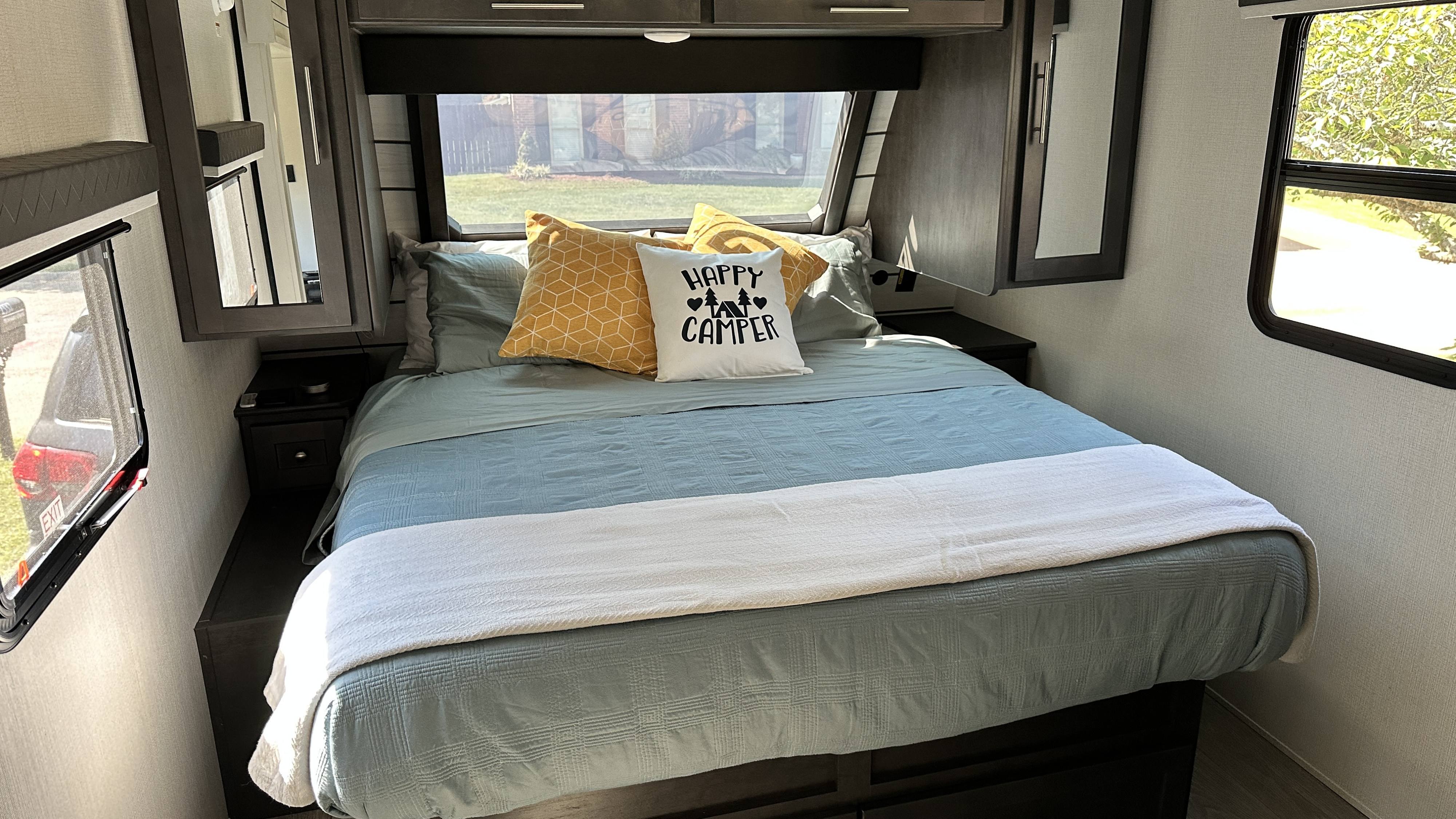 Relax in this inviting RV rental bedroom. Features a comfortable bed, 'Happy Camper' pillow, and practical storage.. Keystone Cougar Half Ton (22MLS) 2025