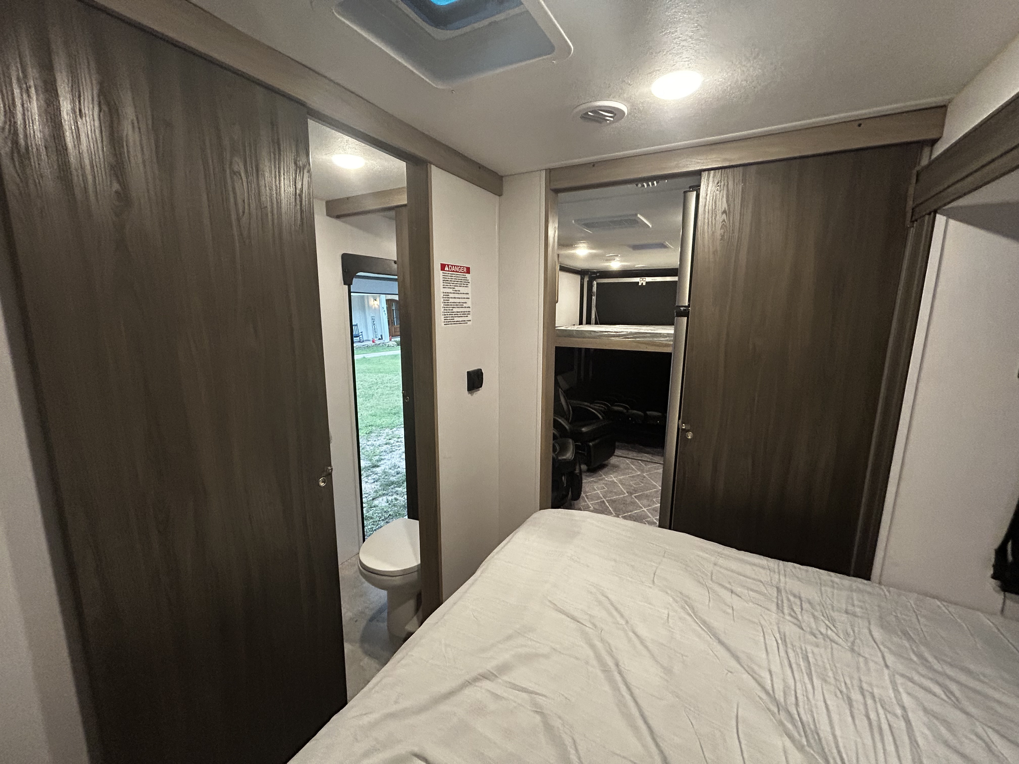 RV rental interior featuring a comfortable bed, peek into the bathroom with a toilet, and a bunk room with recliners.. Work and Play Toy Hauler 2022