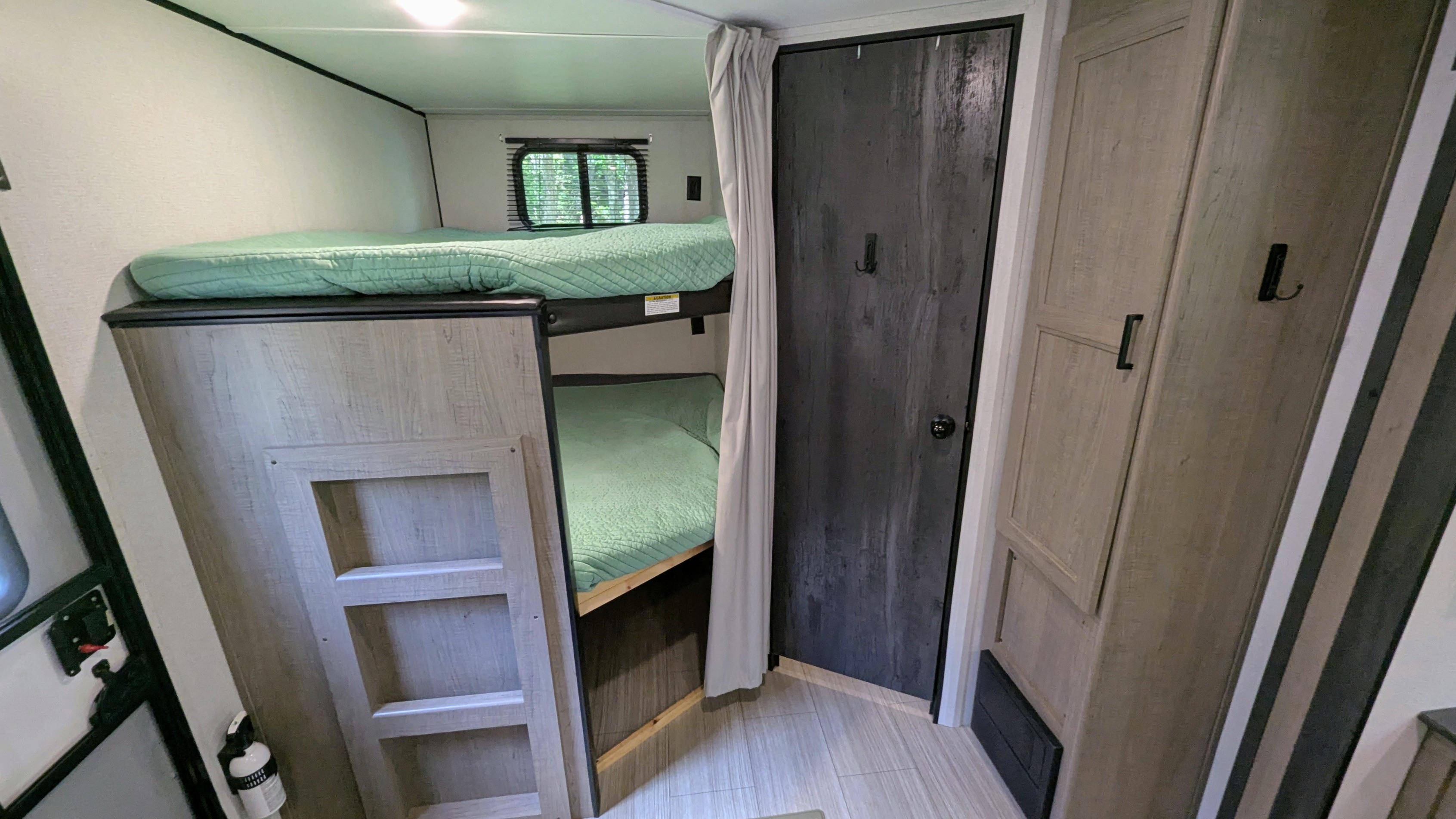 rv rental: Interior view of bunk beds with light green bedding, dark door, and wood-grain cabinets. A compact sleeping area.. Keystone Hideout 2021