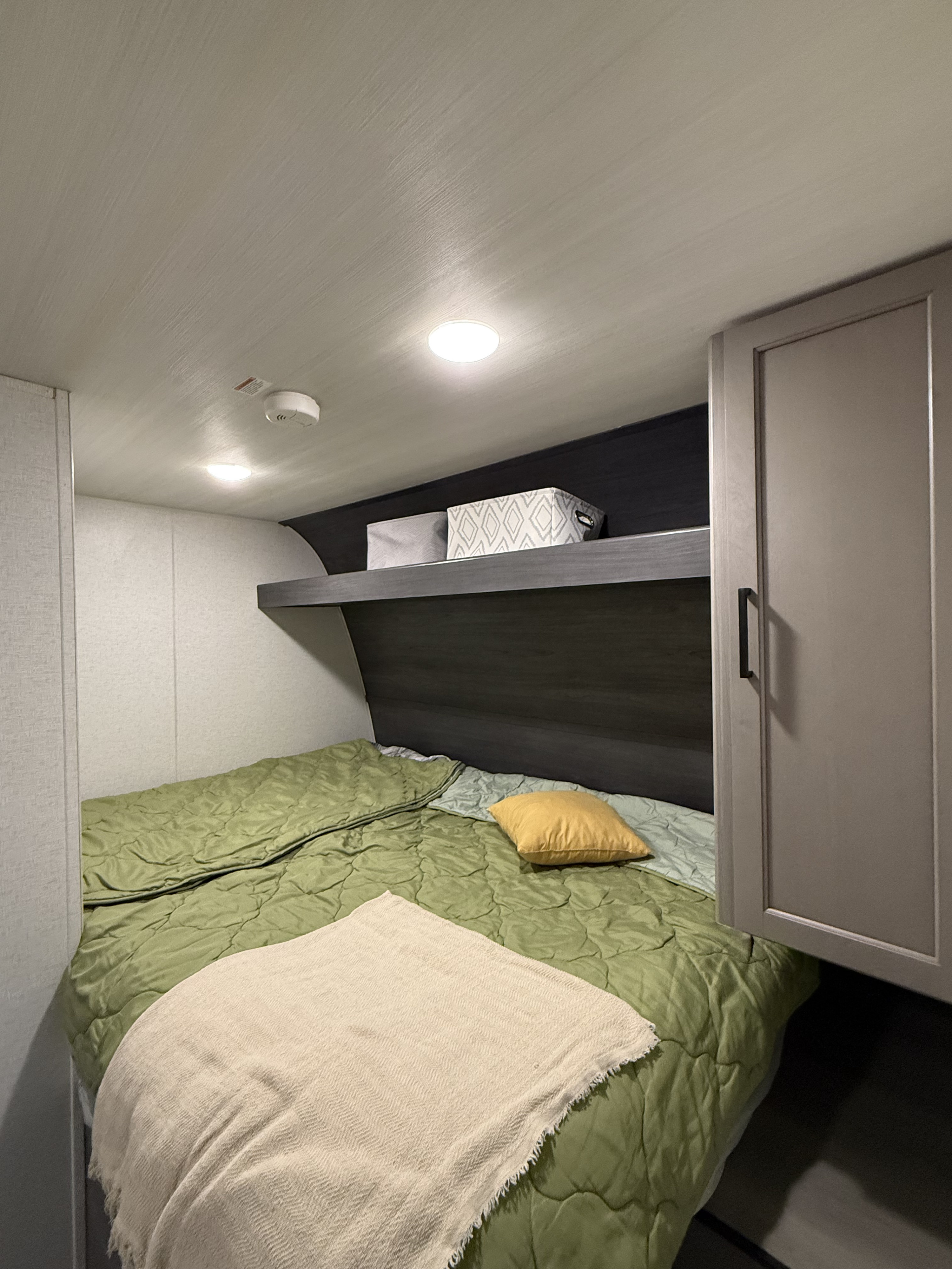Cozy RV rental bedroom featuring a green comforter, yellow pillow, storage shelf with bins, and integrated lighting.. Keystone RV Hideout Sport 2024