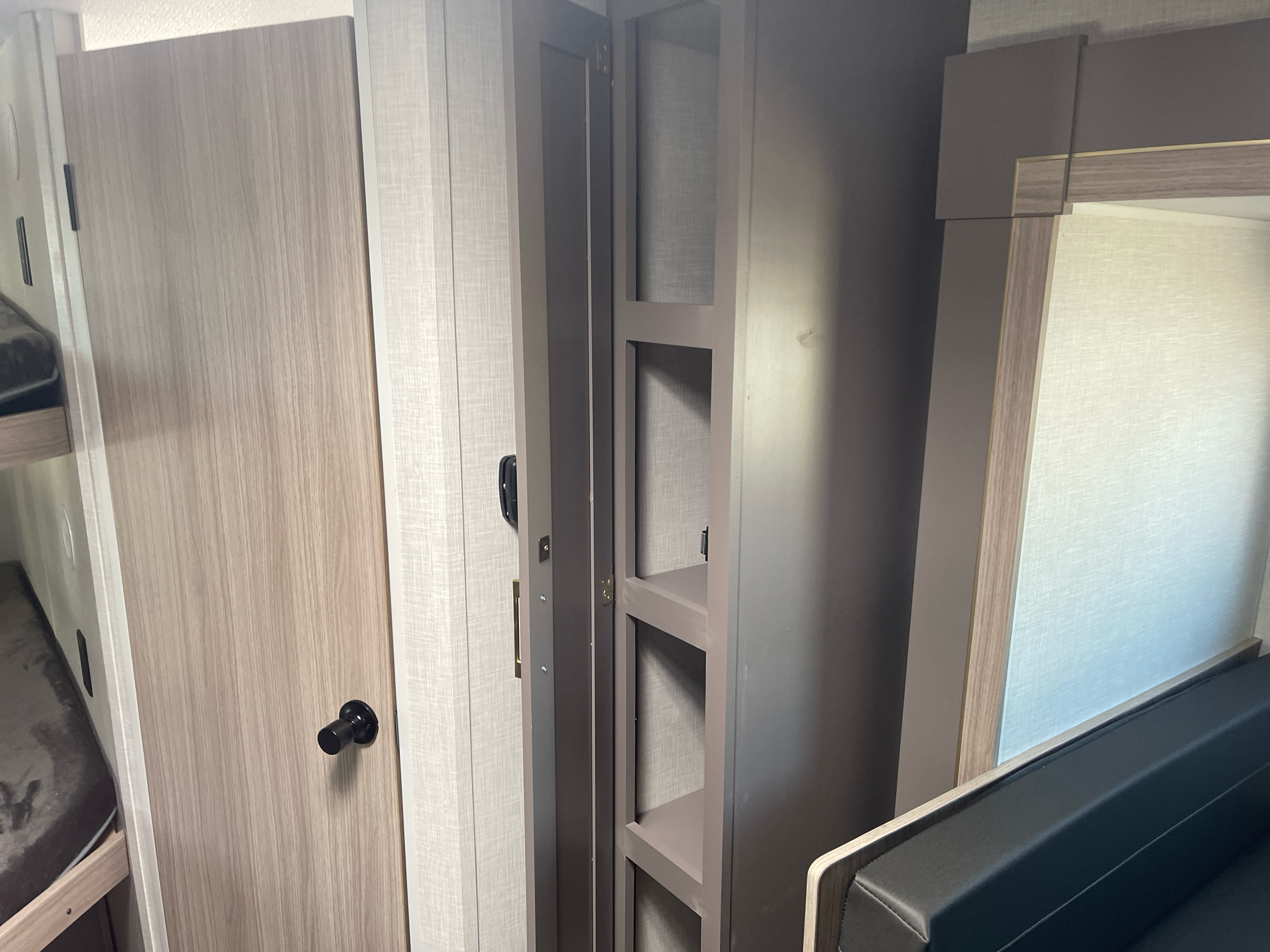RV rental interior showing a light wood door, open storage shelves, and dark upholstered seating/bunk bed.. K-Z Manufacturing Sportsman Classic 2026