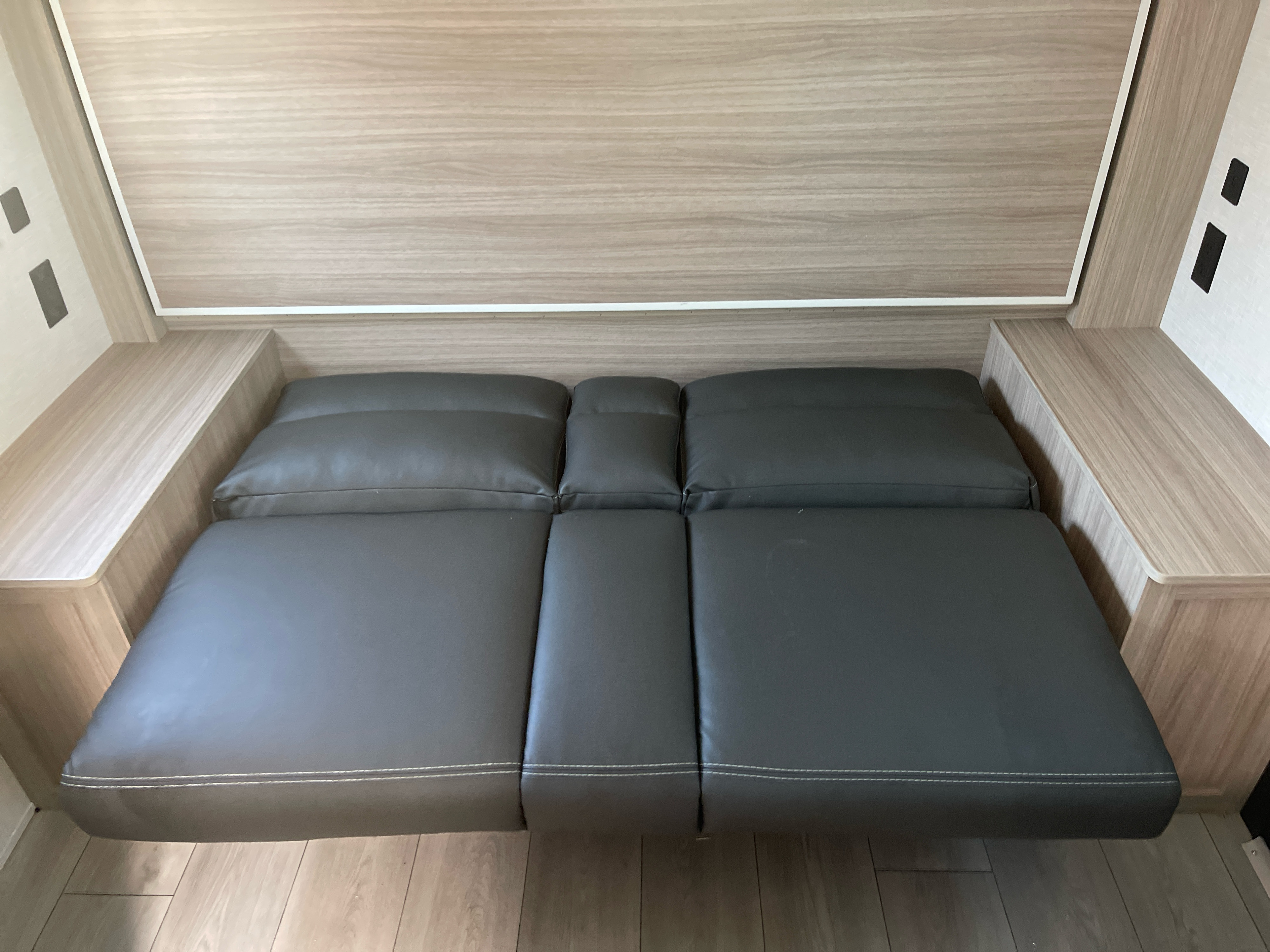 Gray faux-leather convertible bed in an RV rental, flanked by wood grain shelves. Ideal for a modern motorhome sleeping area.. K-Z Manufacturing Sportsman Classic 2026