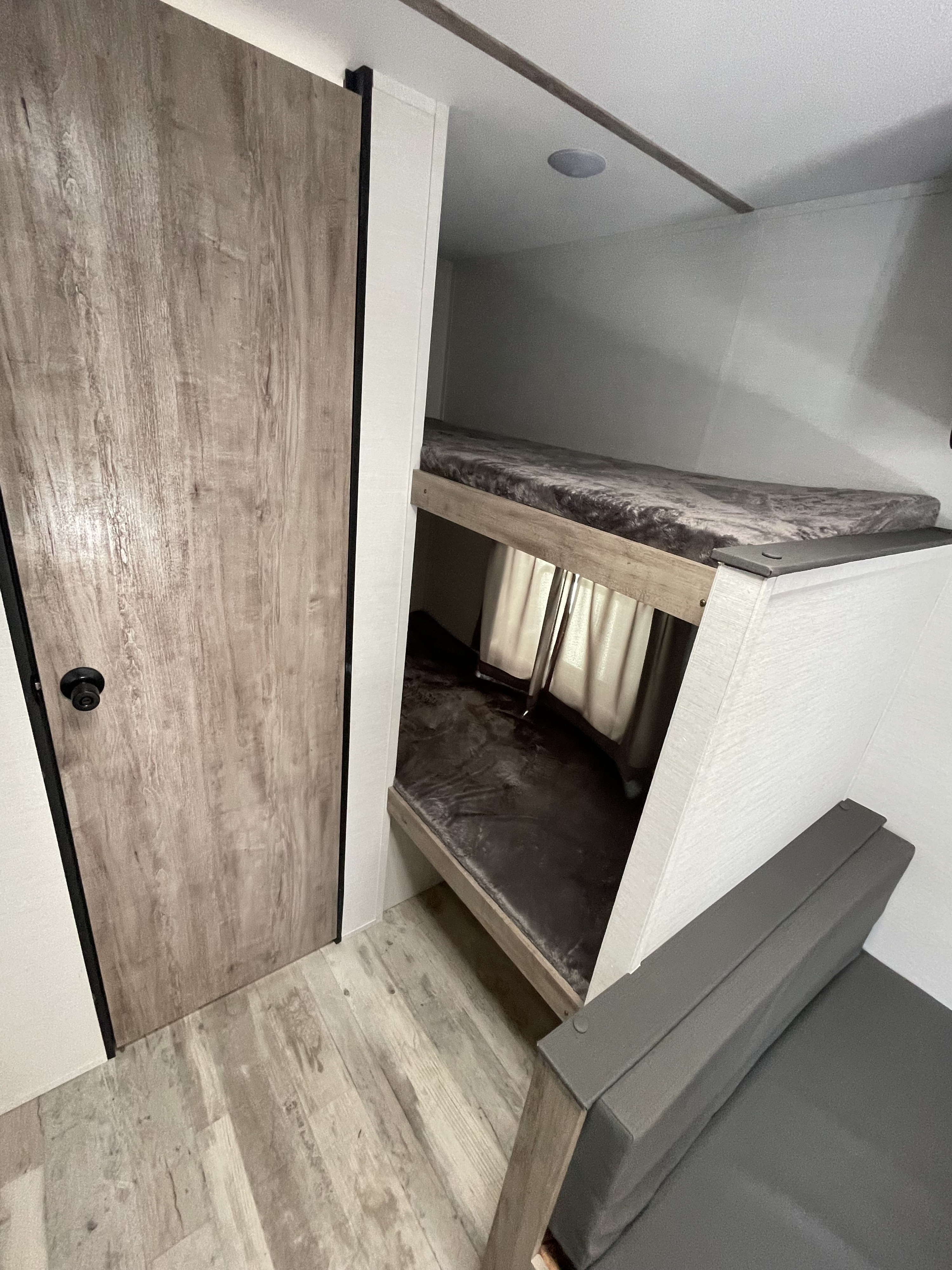 RV rental interior: cozy bunk beds, a grey sofa, wood door, and light wood-look flooring.. Gulf Stream Grand River 2026