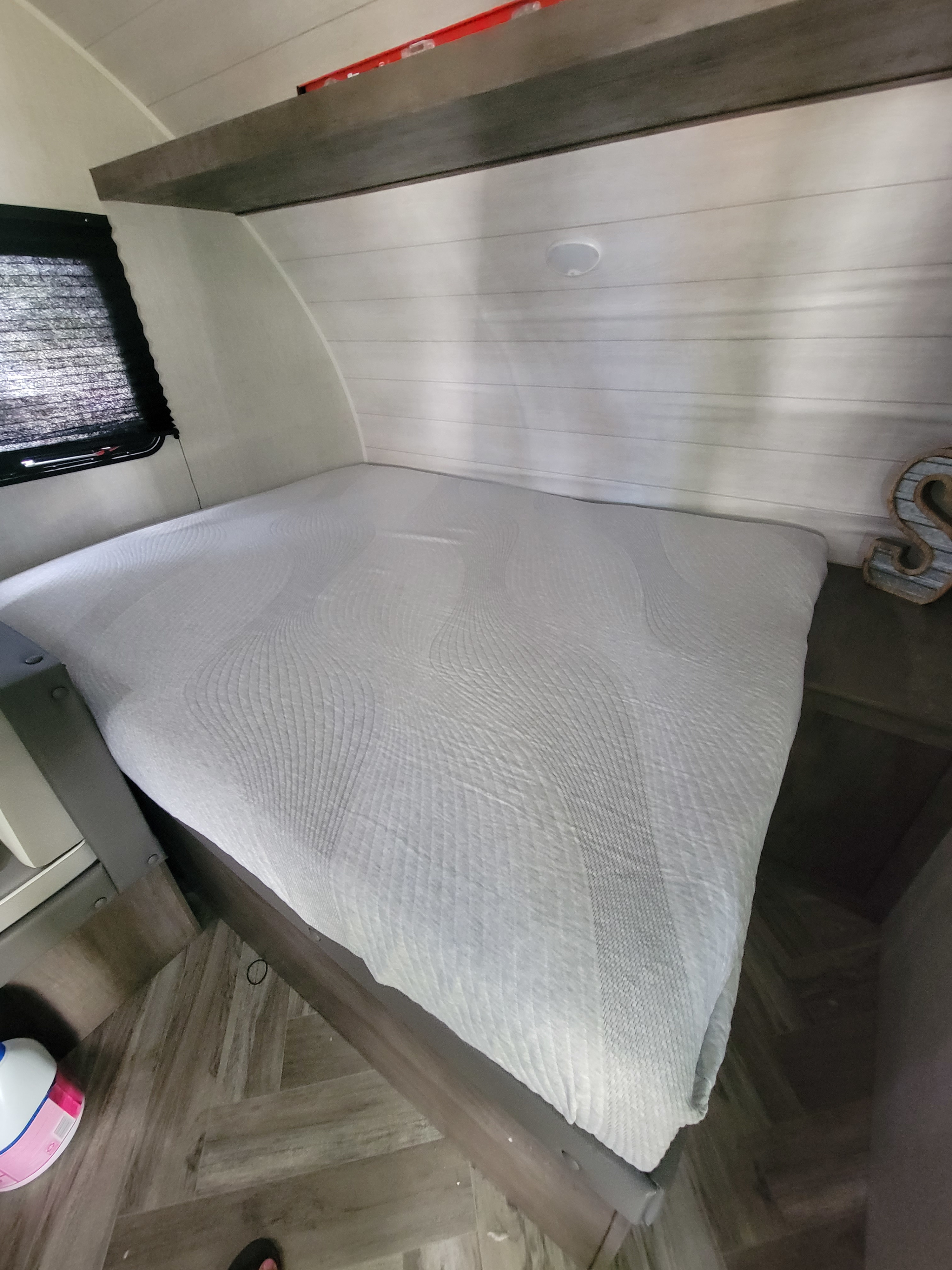 RV rental bedroom: a light-colored, textured bed, window with blinds, wood paneling, and a small shelf. A bottle is on the floor.. Forest River Salem FSX 2021