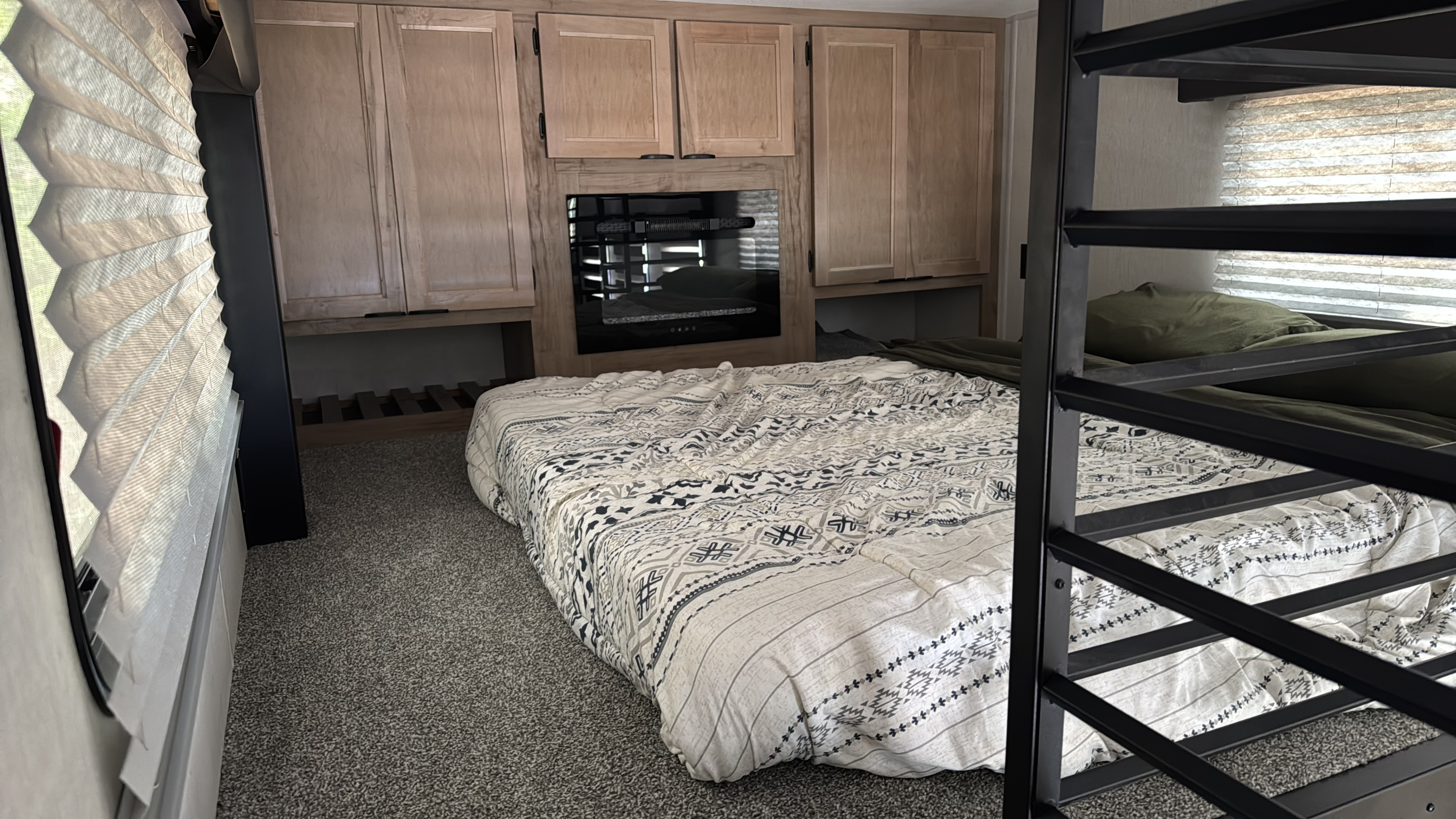 Cozy RV rental bedroom featuring a patterned bed, built-in wooden cabinets, and bunk beds with a metal ladder.. Forest River Timberwolf Mini Loft 2024