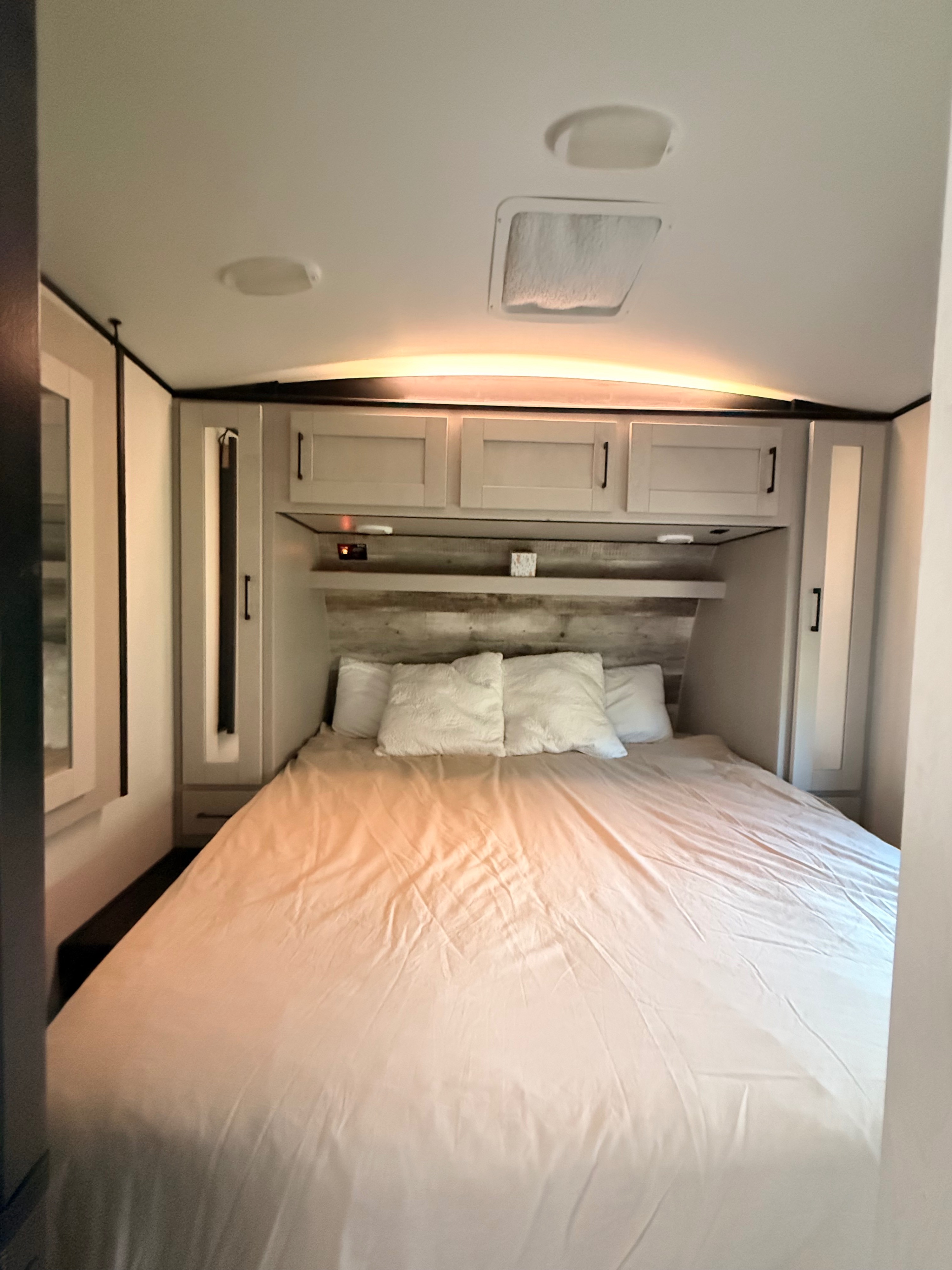 Cozy RV rental bedroom with a comfortable bed, wooden headboard, overhead cabinets, and warm lighting.. Heartland Torque 2021