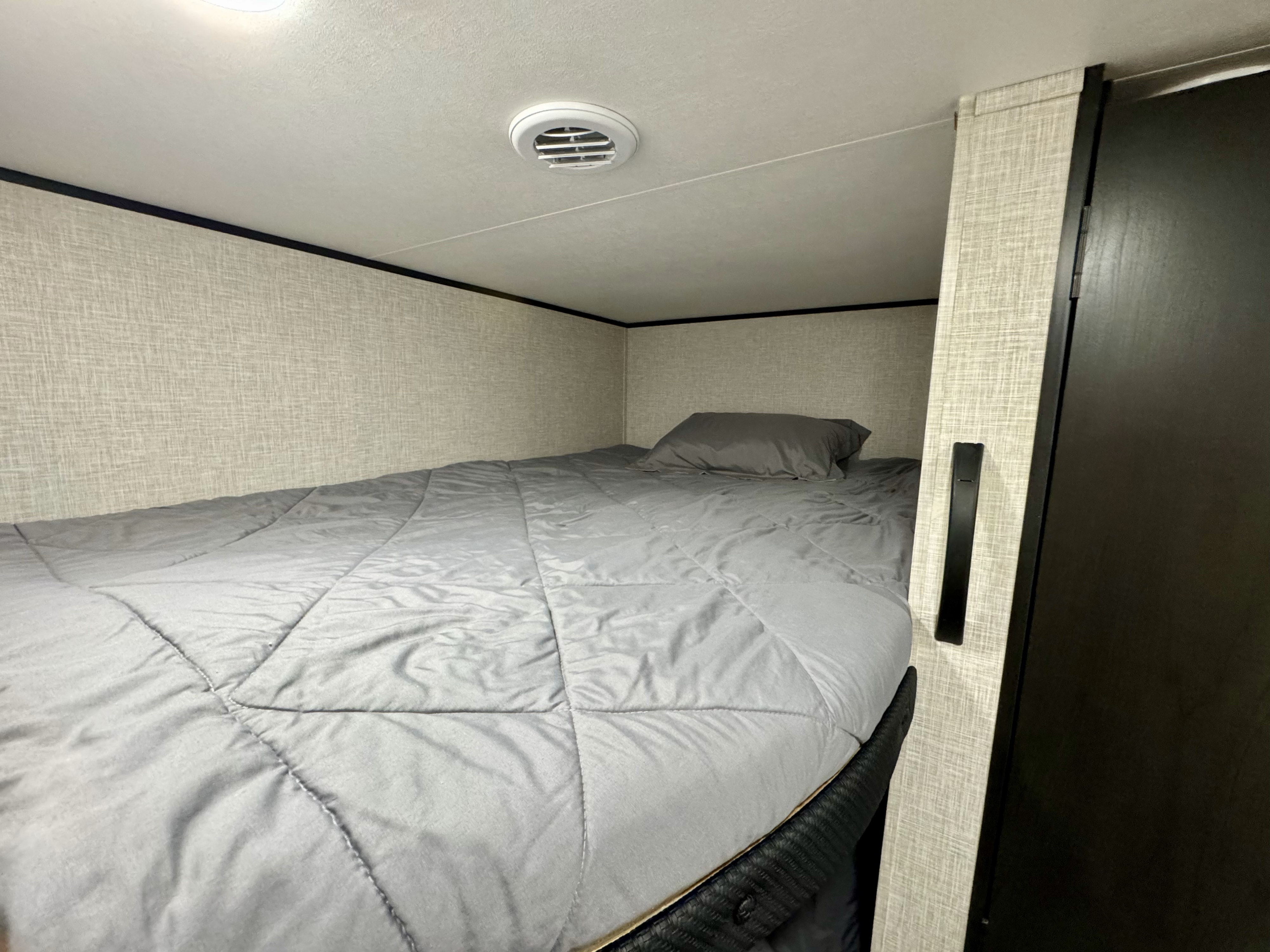 Cozy bunk bed in an RV rental, featuring a gray comforter, pillow, and a ceiling vent for air circulation.. Jayco 260BH 2026