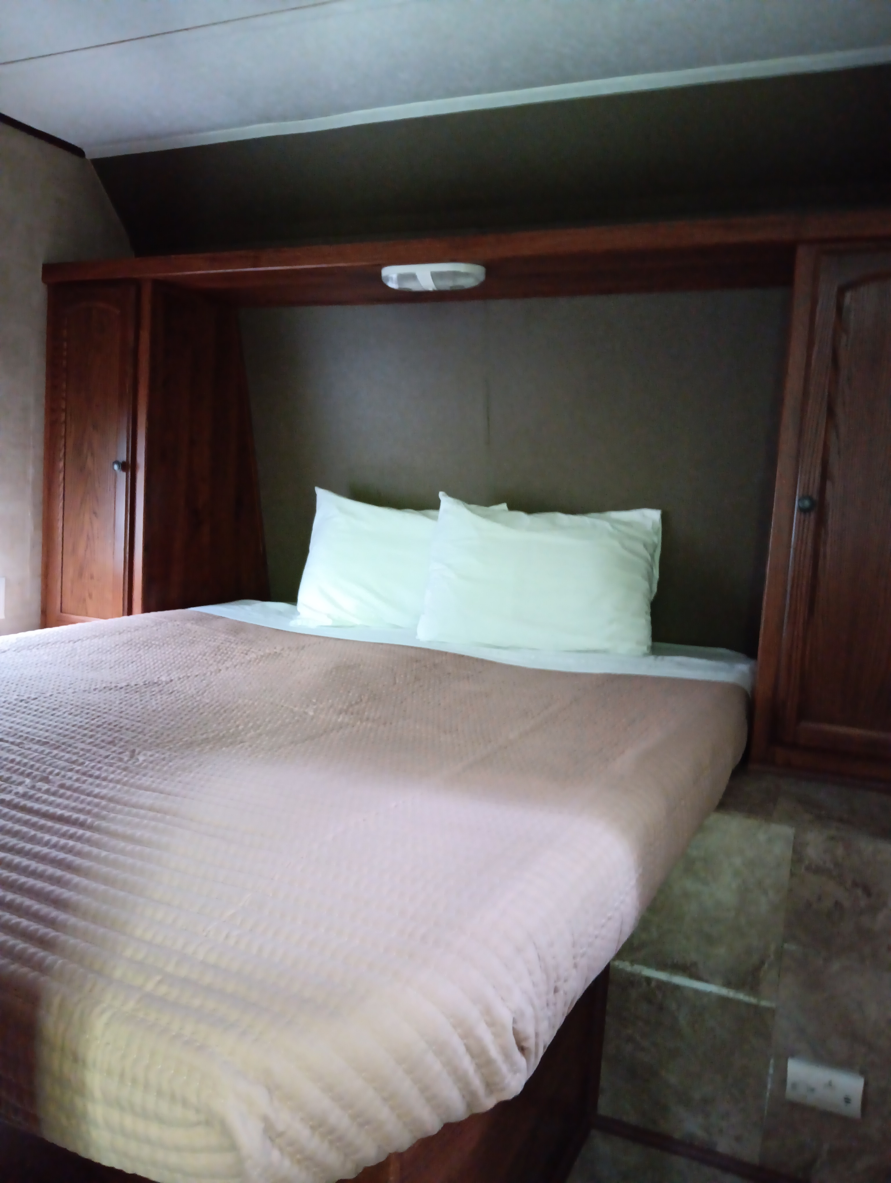 An inviting RV rental bedroom with a made bed, two white pillows, and wood-paneled storage cabinets on either side of the headboard.. Keystone RV Hideout LHS 2013