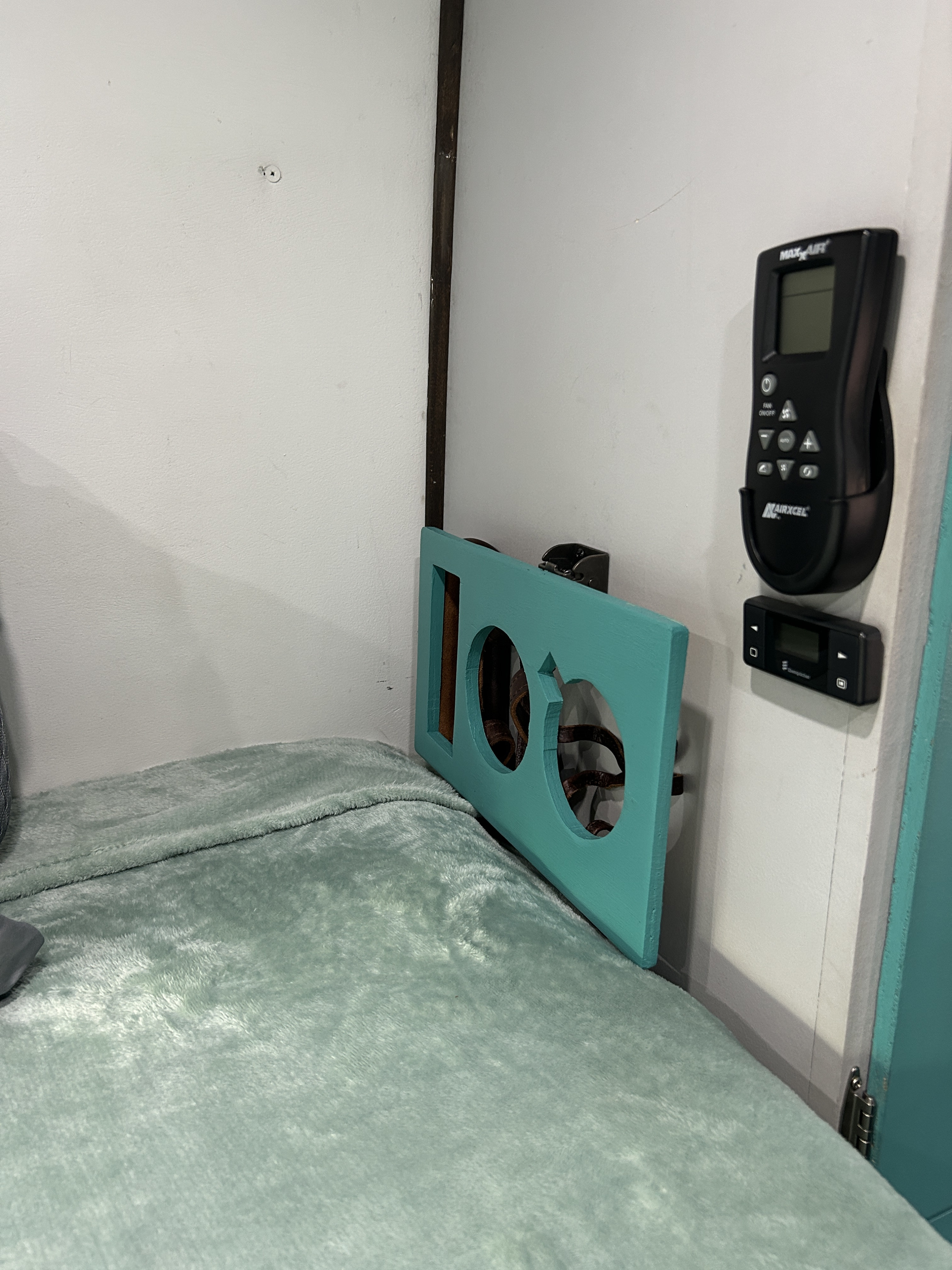 Cozy RV rental interior with a soft green blanket, teal panel, Maxxair remote, and heater control for travel comfort.. Ram Promaster 3500 2018