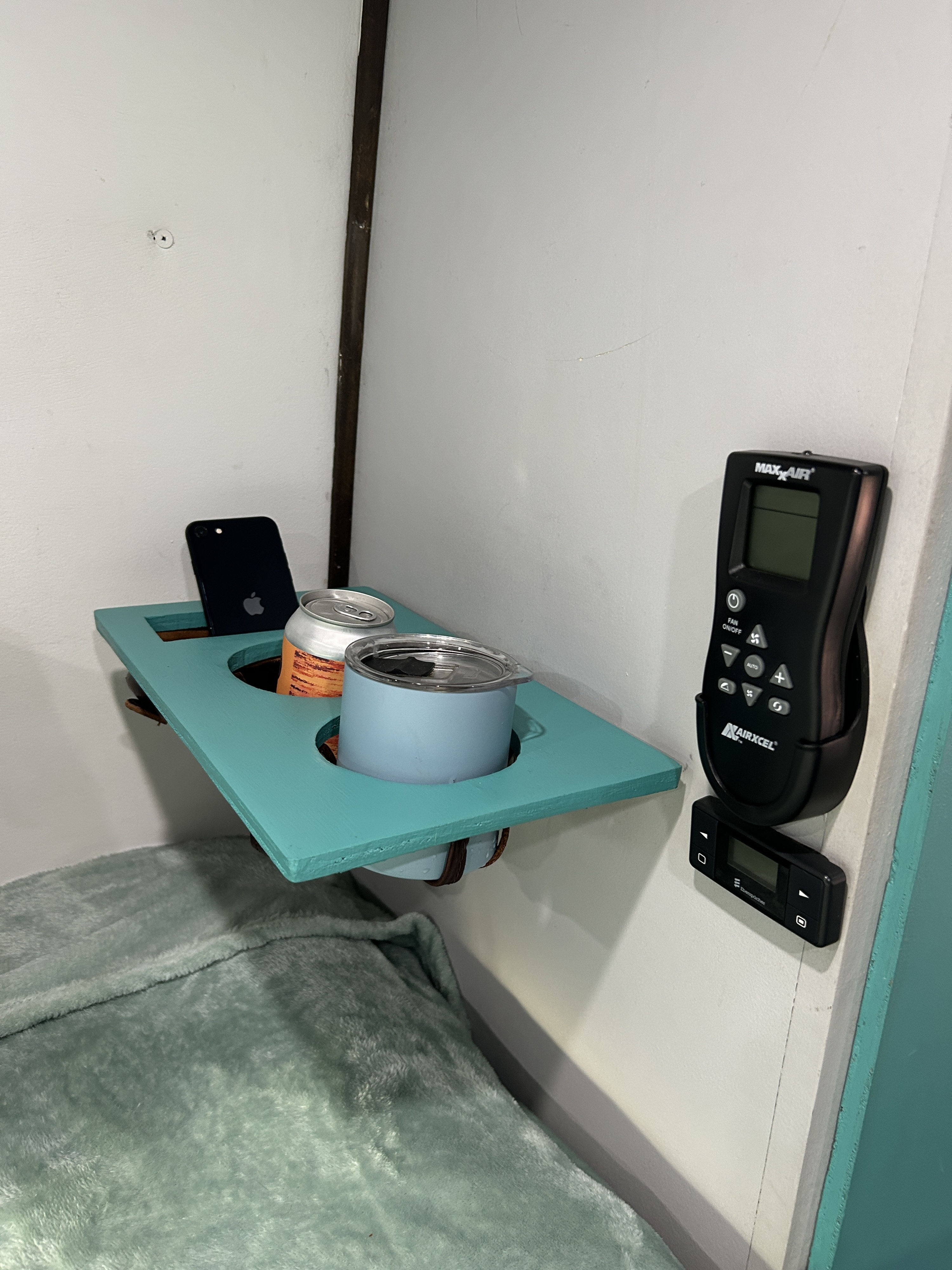 Cozy RV rental bedroom with a teal bedside shelf holding a phone, canned drink, and mug, alongside climate controls.. Ram Promaster 3500 2018