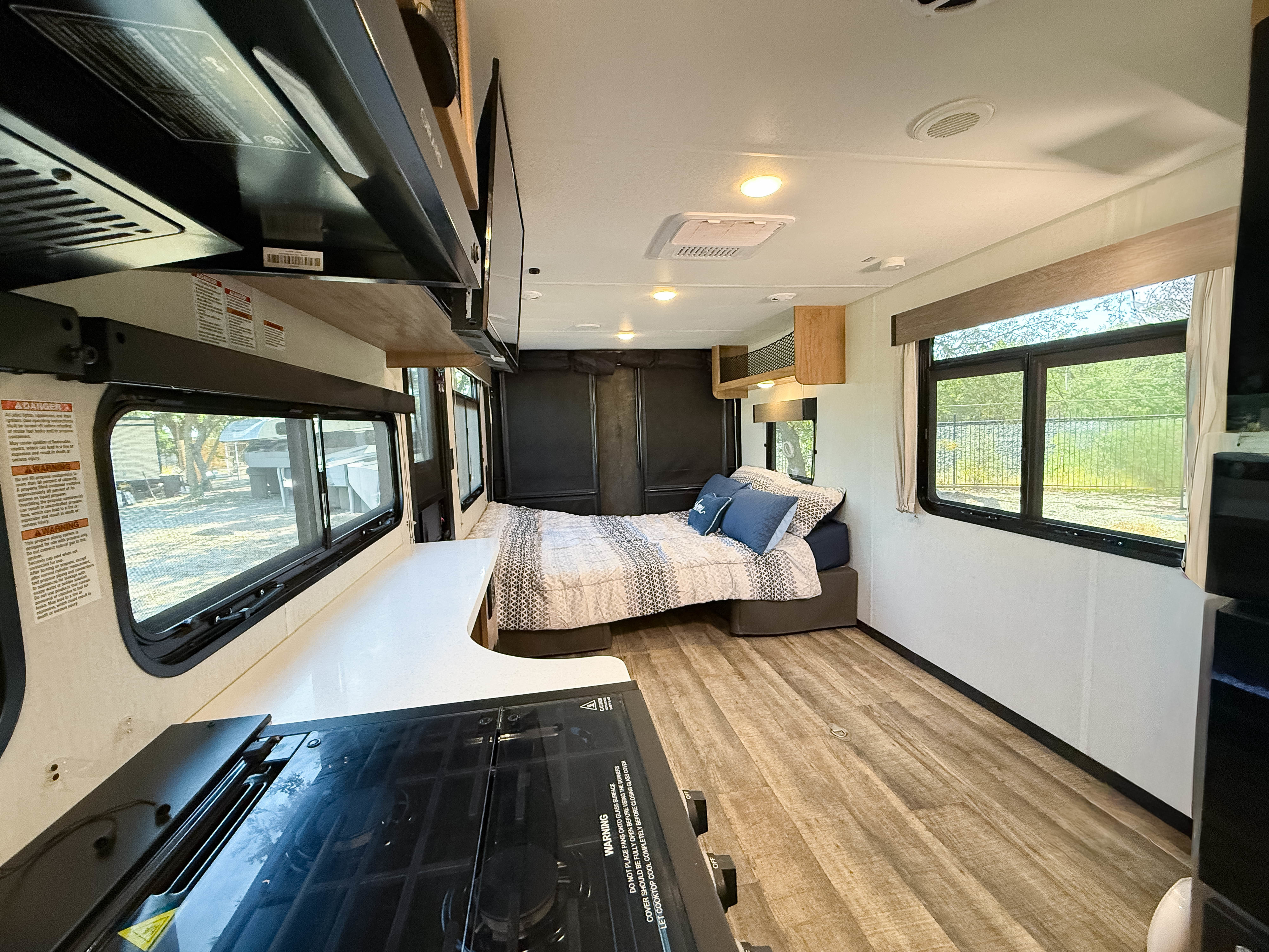 Spacious RV rental interior featuring a cozy bed, modern kitchen with stovetop, and large windows with natural light.. Forest River Black Label 2024