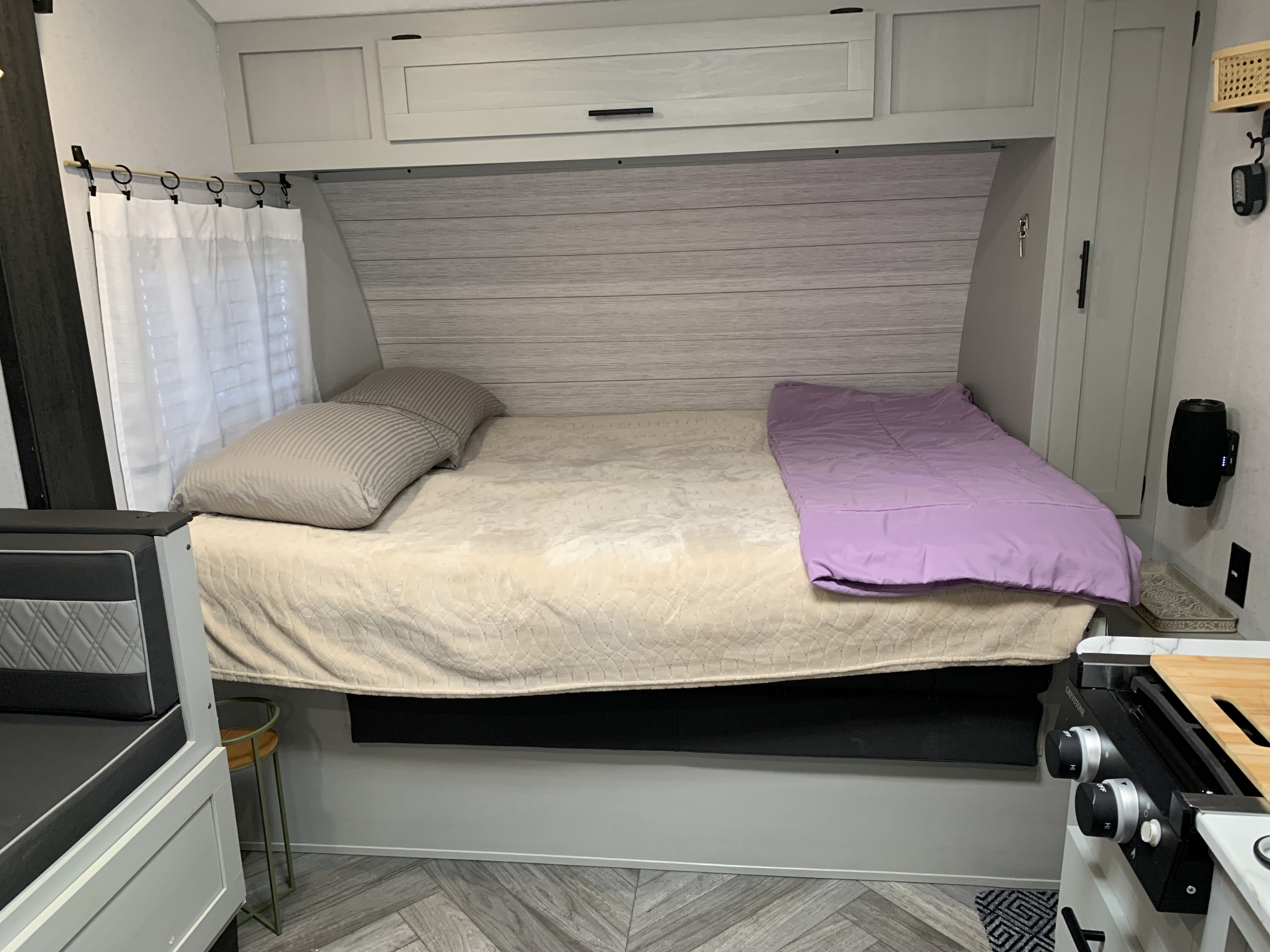 Cozy RV rental bedroom with a bed, striped pillows, lavender comforter, modern cabinetry, and a partial kitchen view.. Forest River Wildwood FSX Plantium 2022