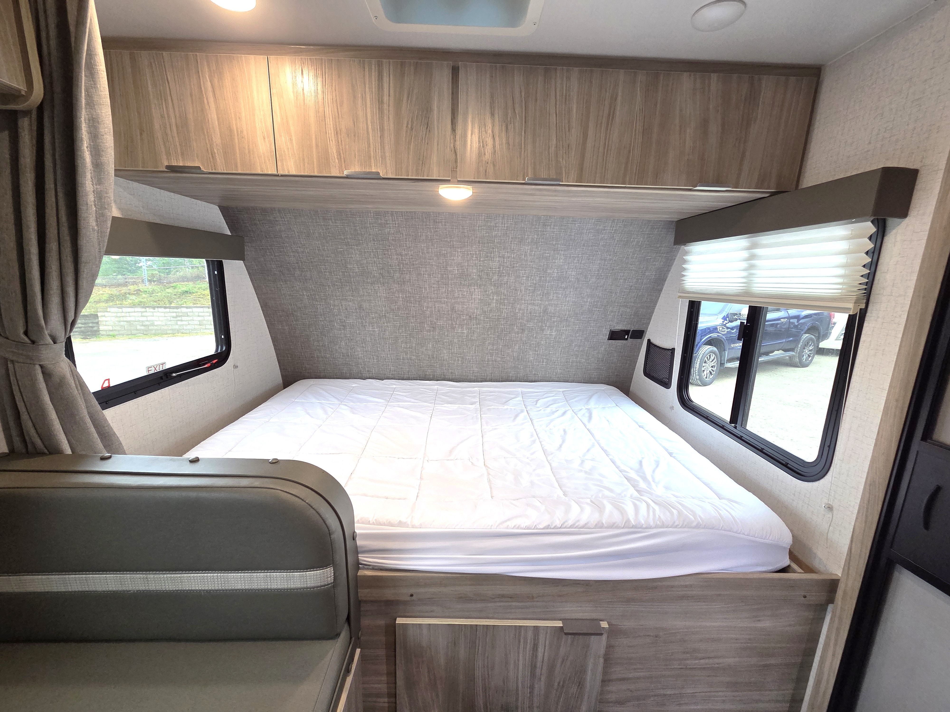 Experience comfort in this RV rental bedroom: a large bed with quilted topper, overhead storage, and dual windows.. Winnebago Micro Minnie 2021