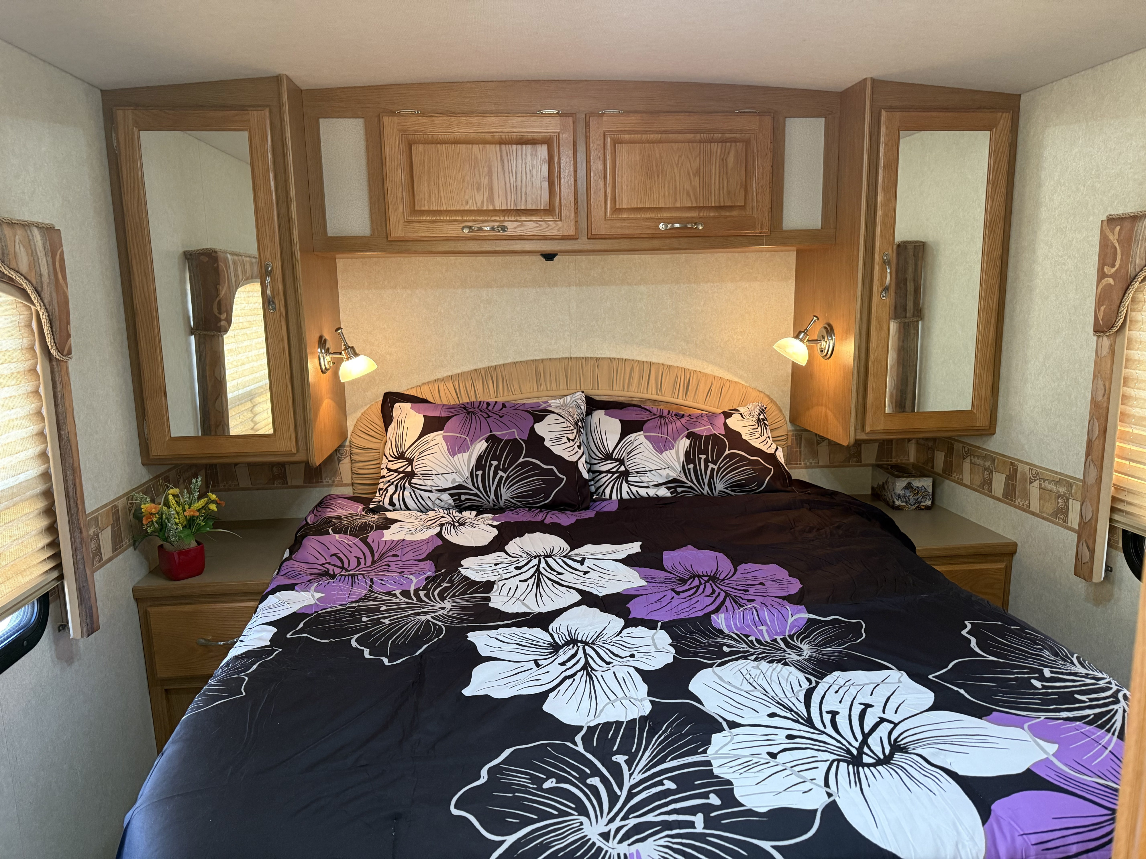 Cozy RV bedroom for your next rv rental adventure, featuring floral bedding, overhead storage, and compact nightstands with reading lights.. Triple E Embassy 2003