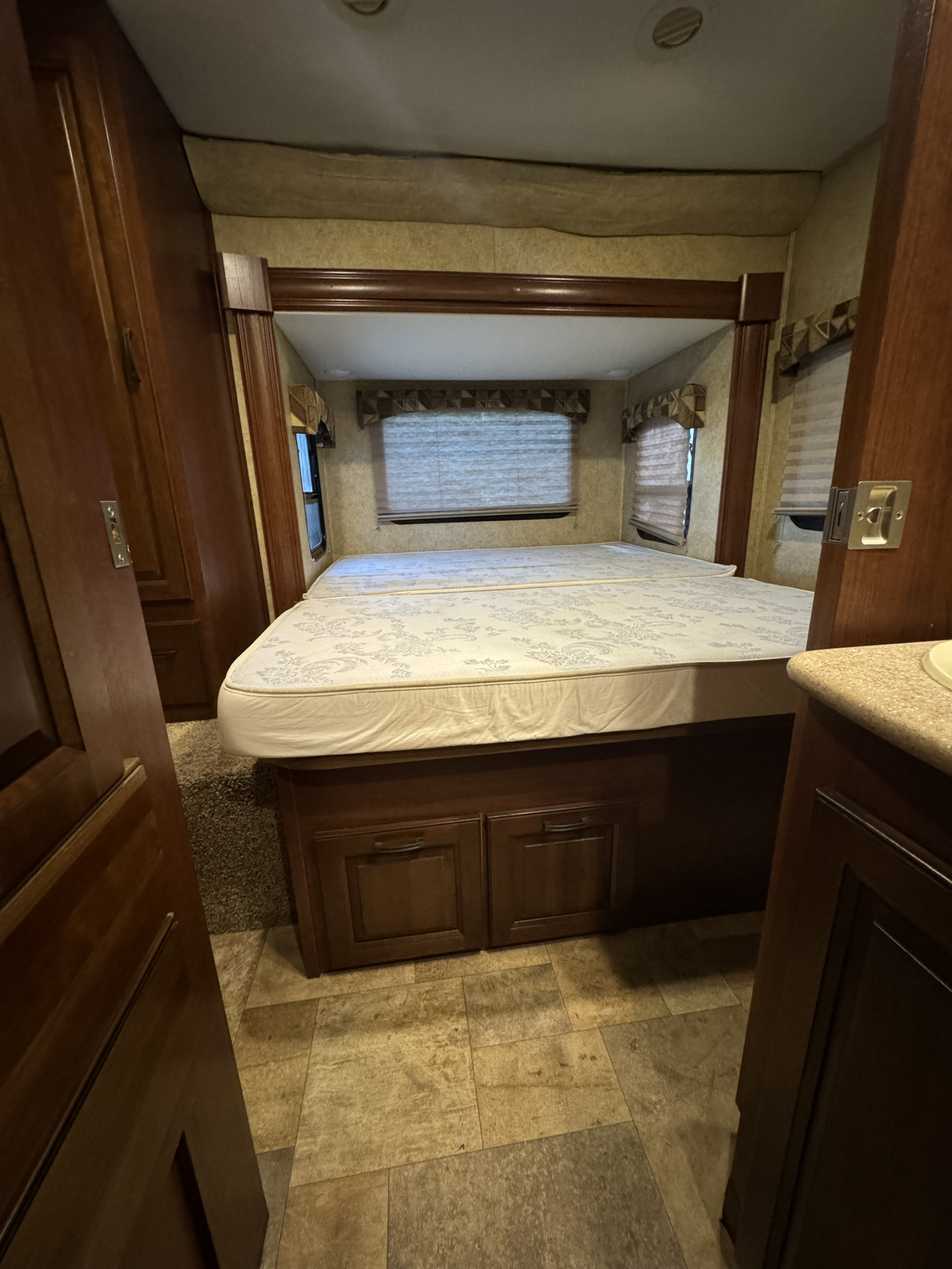 This RV rental's bedroom shows a large bed with under-bed storage, window blinds, and rich wood cabinetry, offering a cozy space.. Forest River Solera 24r 2014