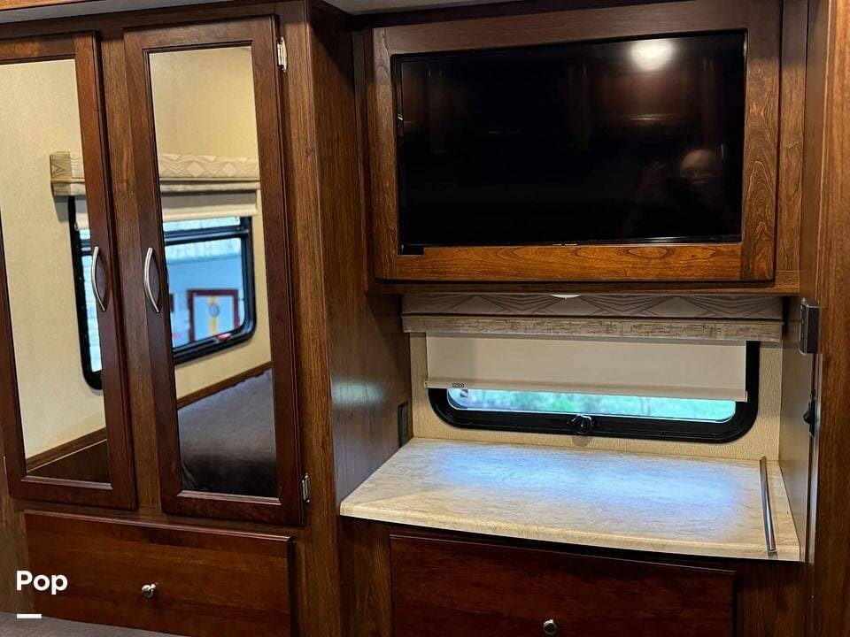 View inside an **RV rental**: wood cabinetry with mirrored wardrobe, mounted TV, and desk space by a window.. Coachmen Pursuit 2019