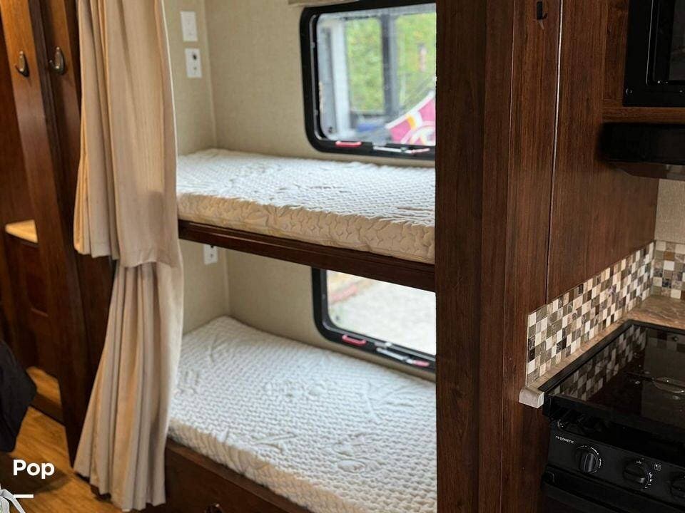Cozy RV rental interior featuring comfortable bunk beds with privacy curtains and a compact kitchen, ideal for travel.. Coachmen Pursuit 2019