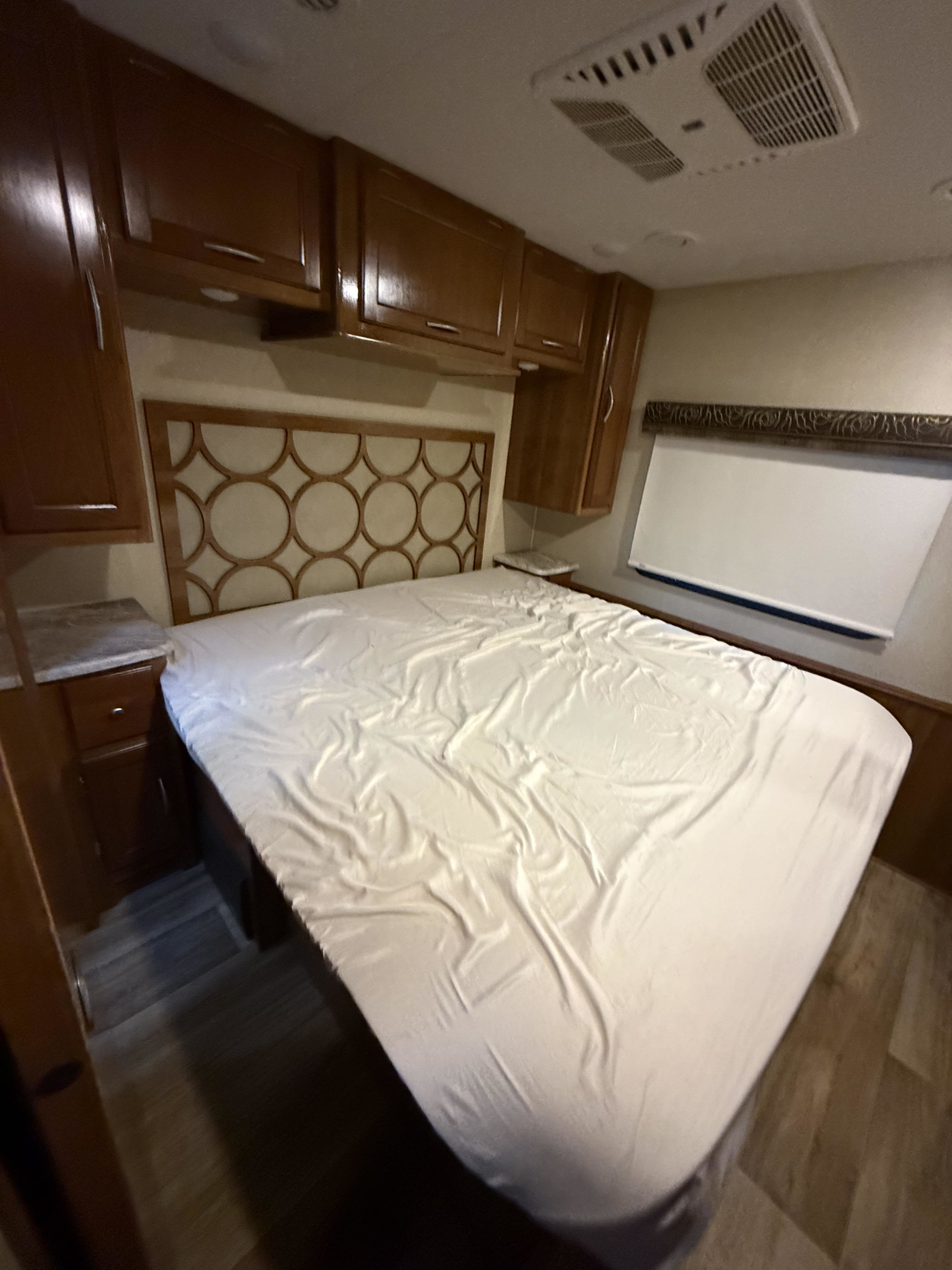 RV rental bedroom: a cozy bed with white sheets, patterned headboard, wooden overhead cabinets, and a window for comfortable stays.. Coachmen Pursuit 2019