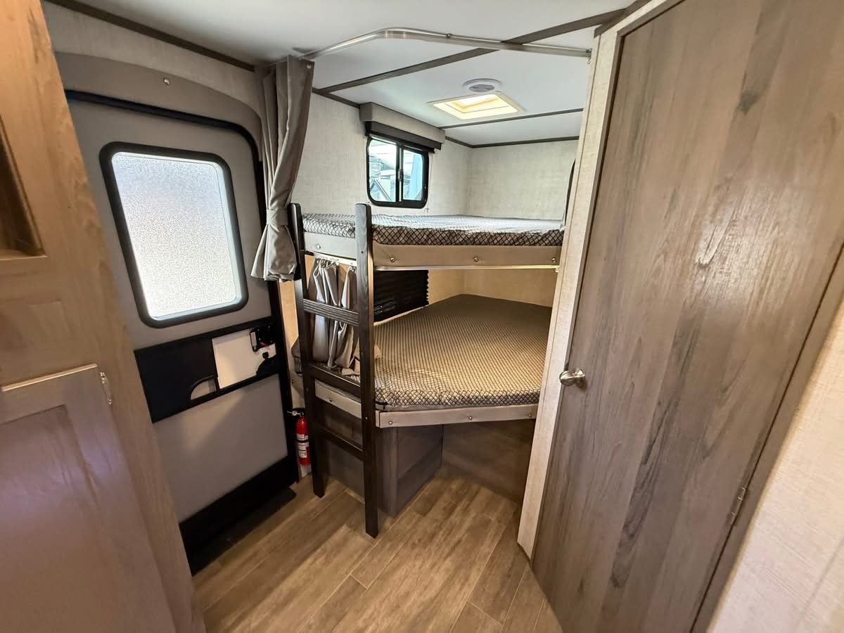 Inside this RV rental: comfortable bunk beds, an entry door to the left, and a wooden interior door to the right for family camping.. Gulf Stream Envision 2023