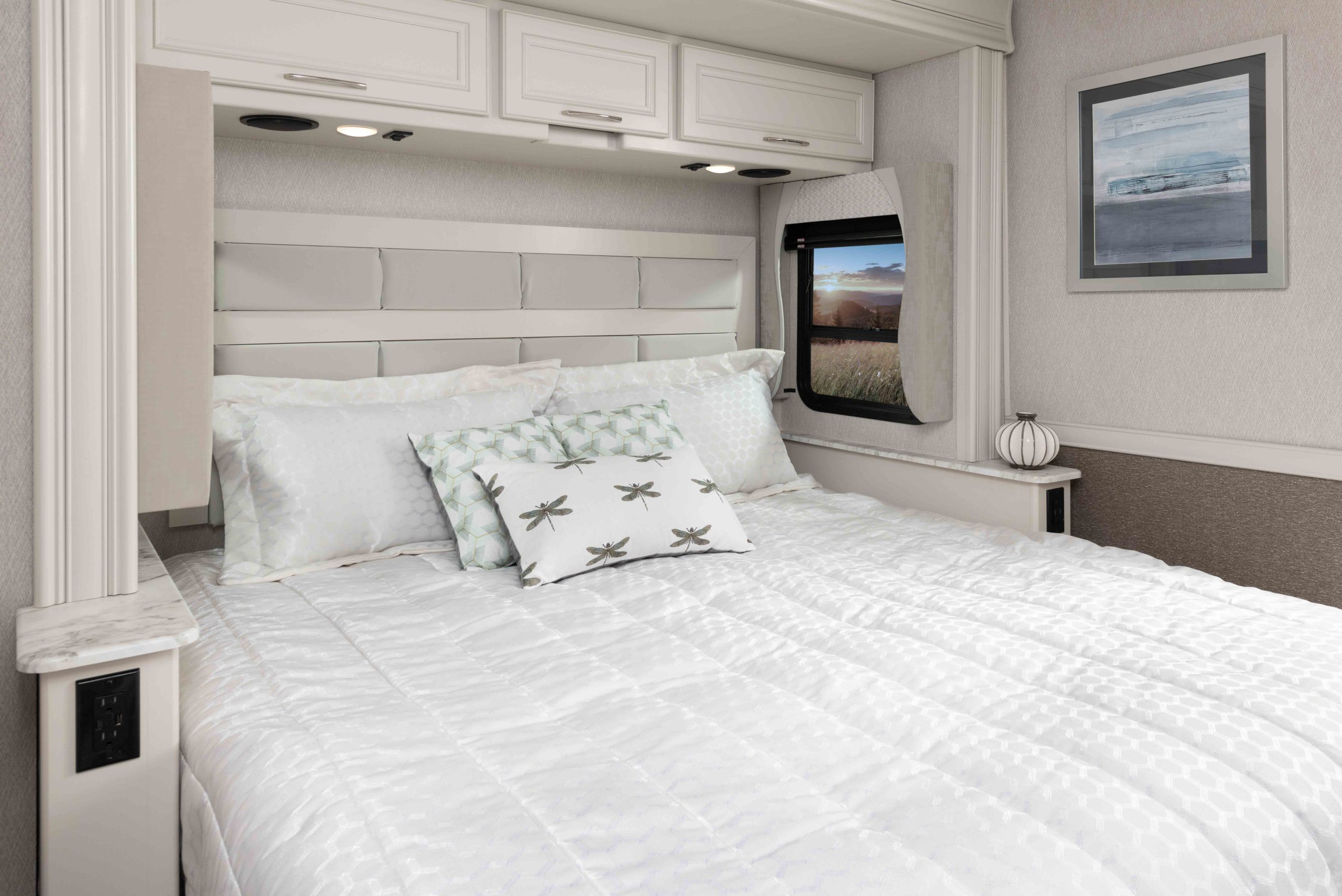 Cozy RV rental bedroom featuring a comfy bed, padded headboard, overhead storage, and a scenic window view.. Fleetwood Bounder 2023