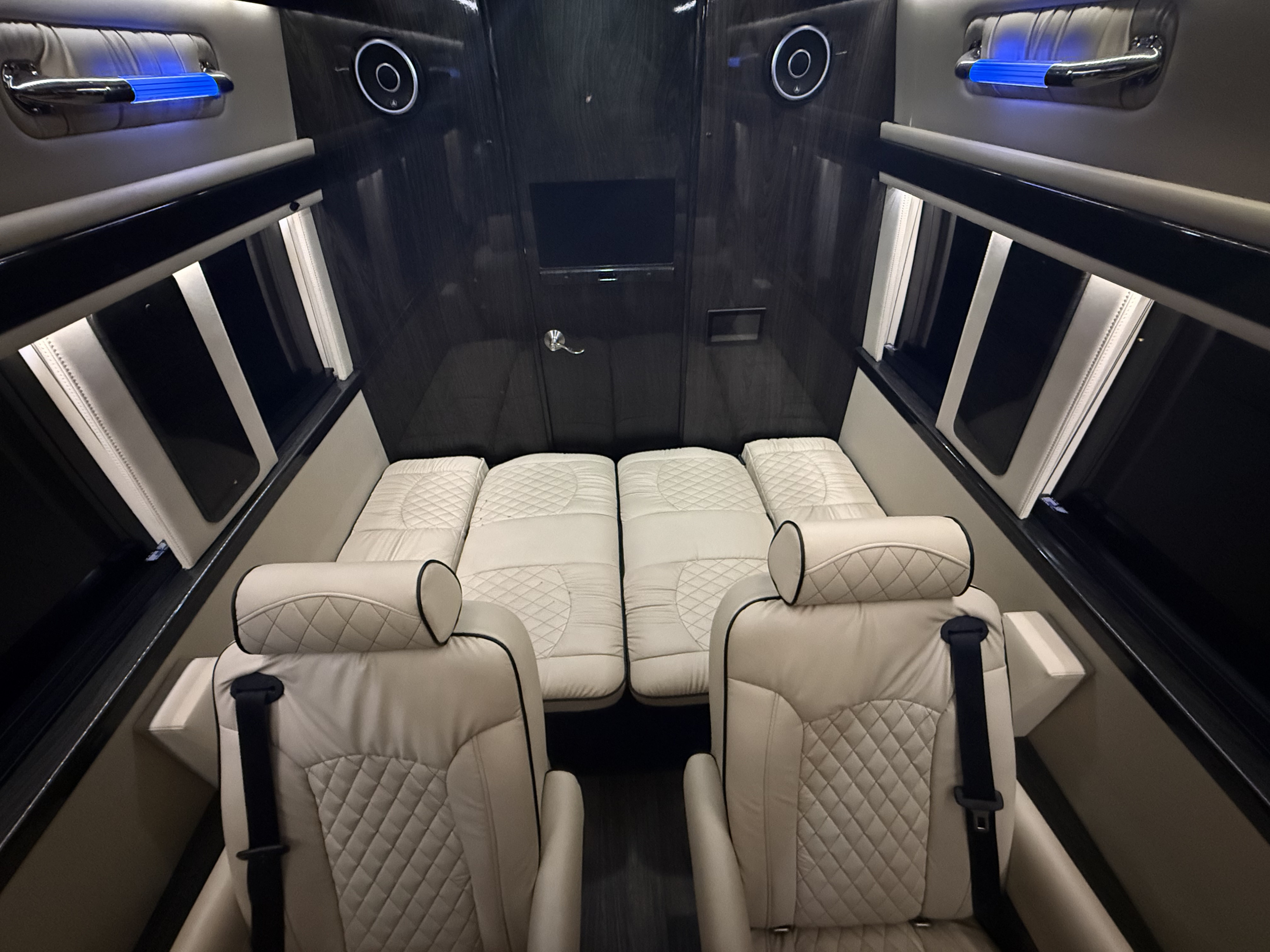 Luxury RV rental interior: cream quilted captain's chairs, convertible bed, dark wood walls & ambient lighting.. Ultimate Toys Ultimate Coach 2023