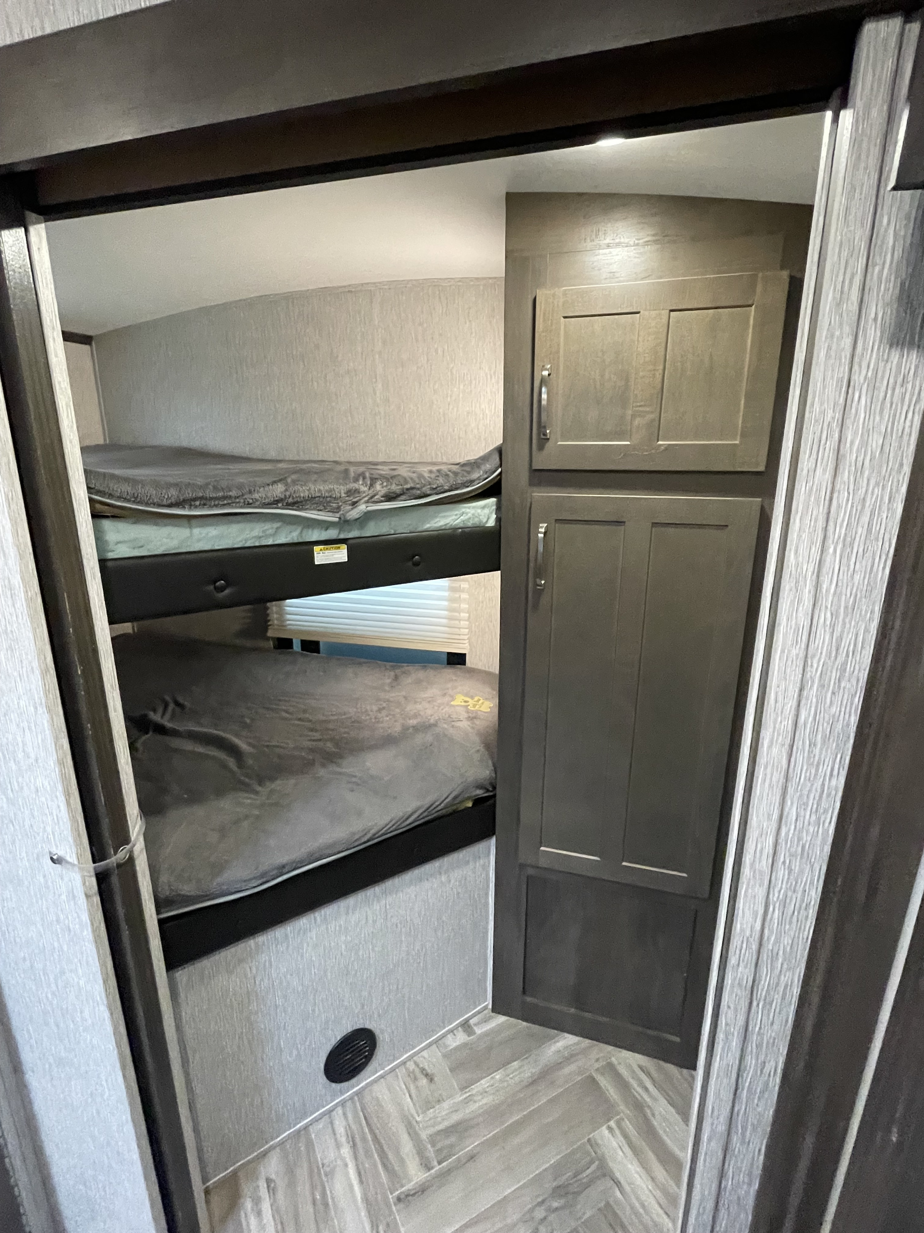 Inside an RV rental: view of bunk beds with gray bedding, a tall storage cabinet, and herringbone flooring in a compact space.. Dutchmen 2903bh 2020