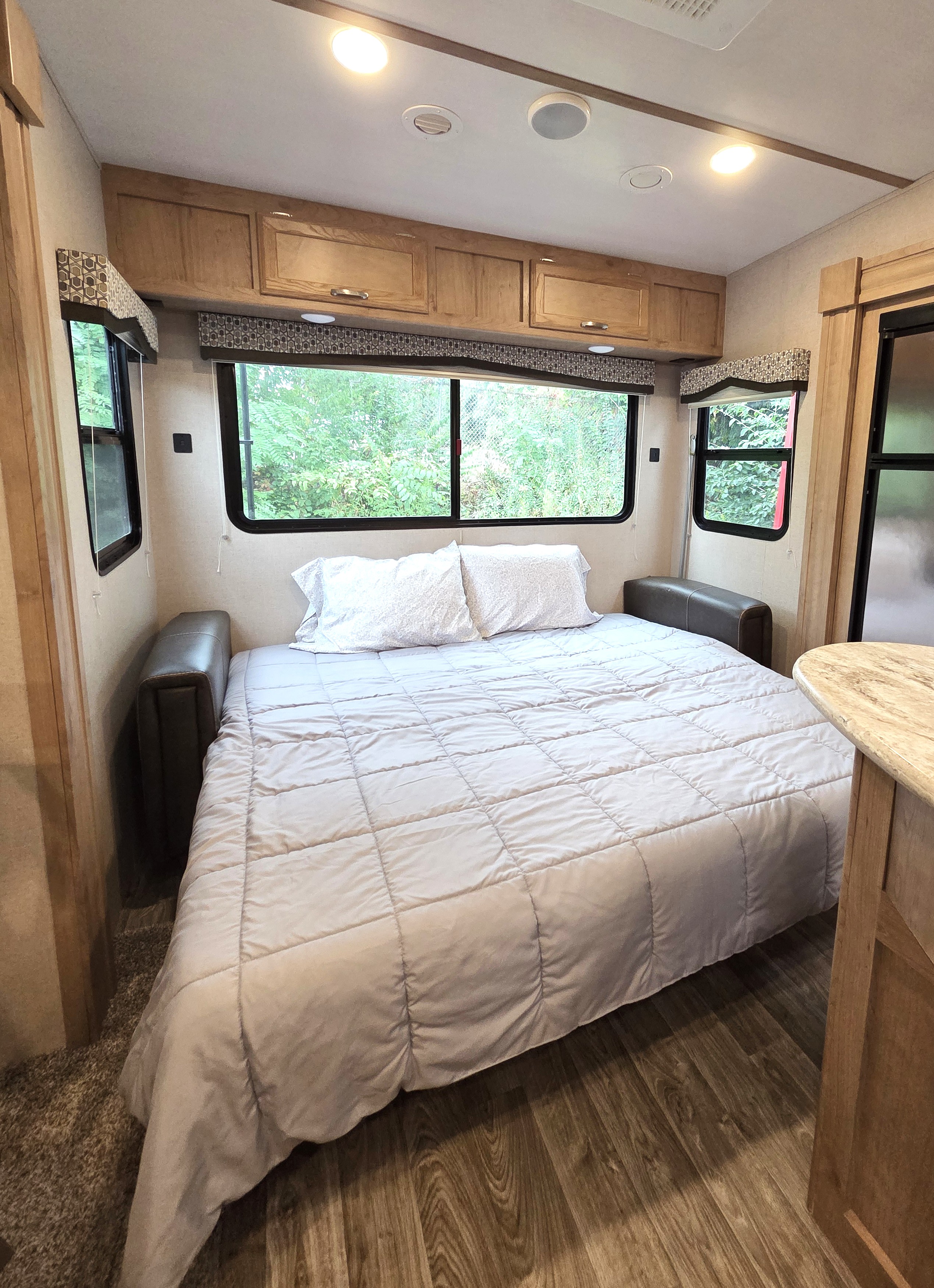 Cozy RV rental bedroom with a made bed, overhead cabinets, & windows showcasing nature.. Winnebago Minnie Winnie 2020
