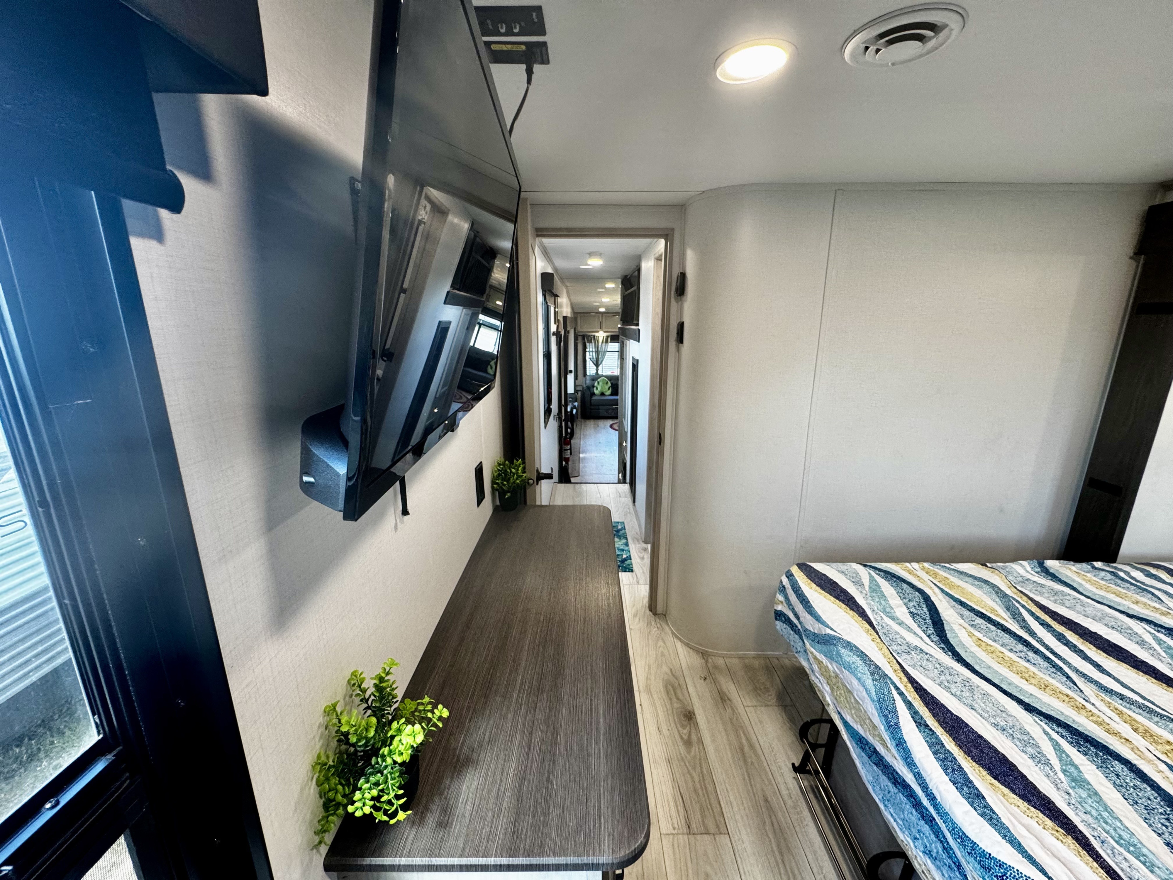Spacious RV rental bedroom and hallway with a mounted TV and comfortable bed, showcasing modern interior design.. Keystone RV Montana High Country 2024