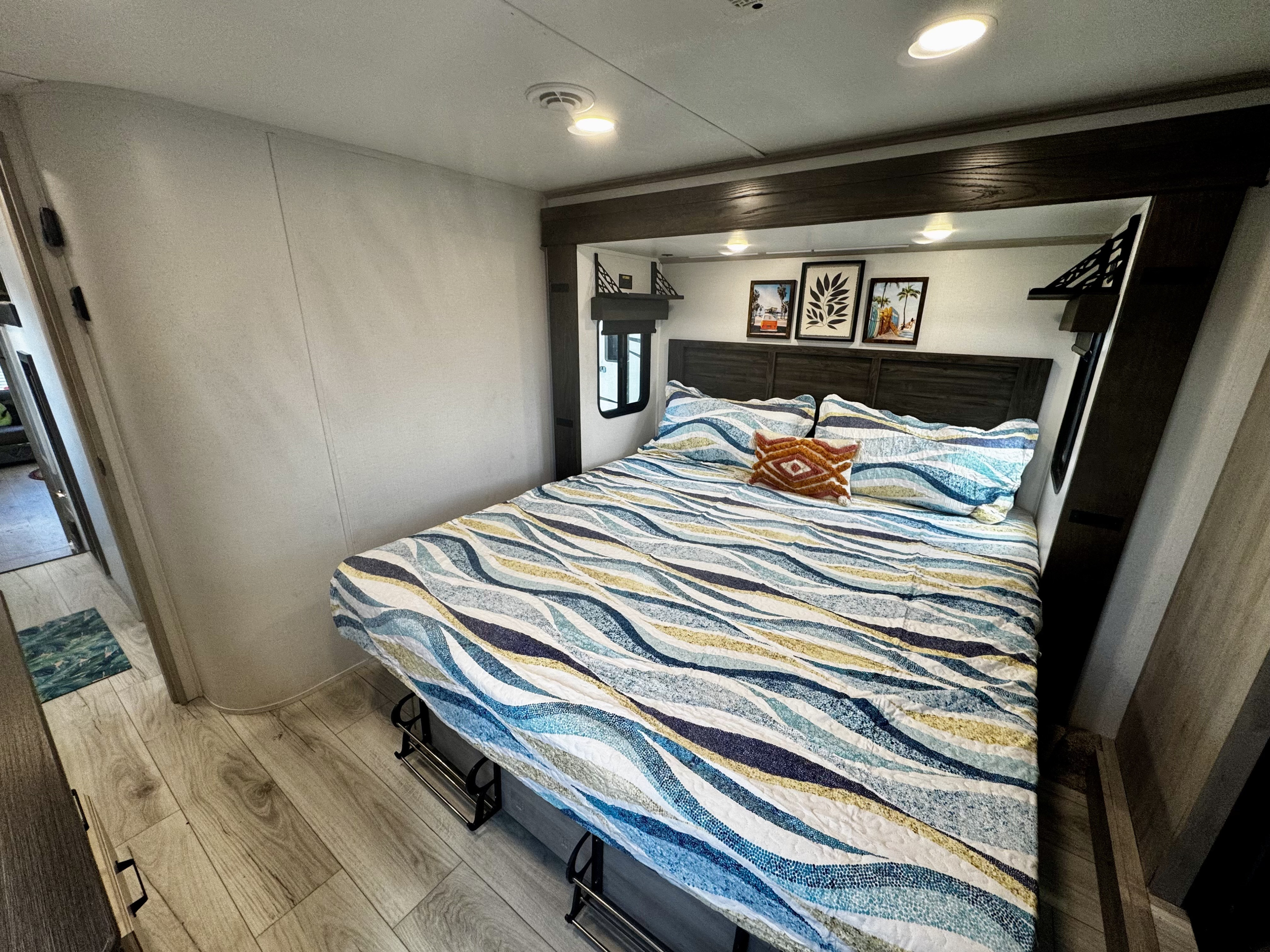 Comfortable RV rental bedroom features a vibrant patterned bed, decorative art, and handy under-bed shoe storage for travel.. Keystone RV Montana High Country 2024