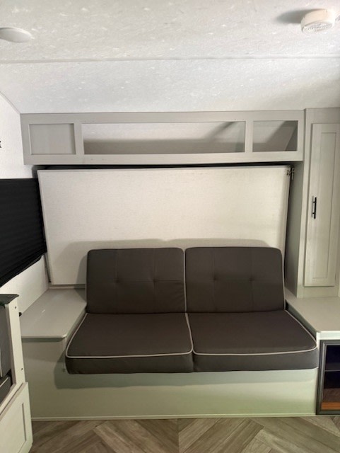 RV rental's compact living area: dark gray sofa, overhead cabinet, and a folded-up Murphy bed for maximizing space.. Forest River Salem 2022